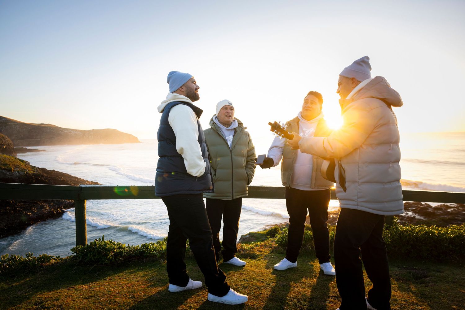 People gathered along a rocky coastline watching the golden sunrise over the Pacific Ocean.