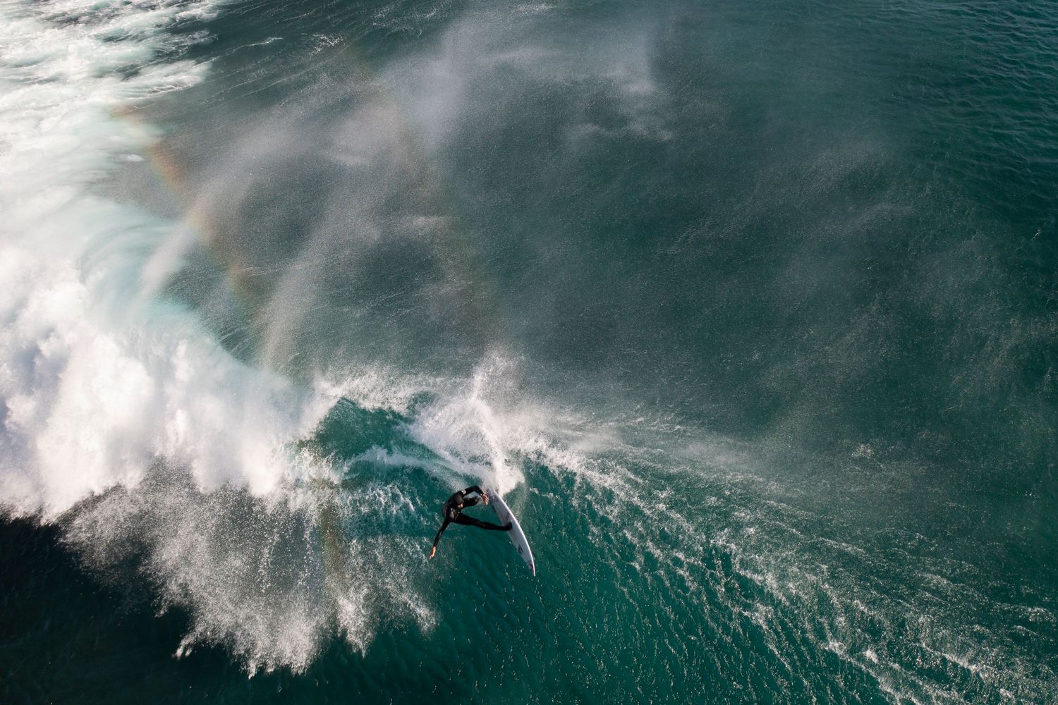 Aerial view of massive ocean waves crashing with white foam against turquoise waters.