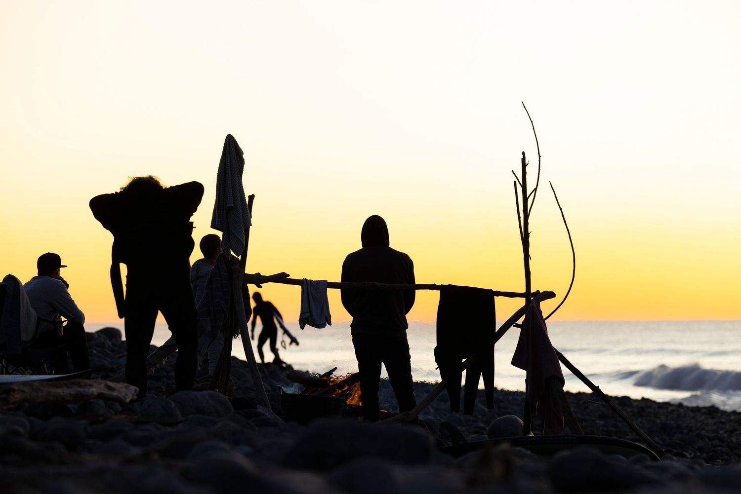 Silhouettes of people against a vibrant orange sunset sky on a beach.