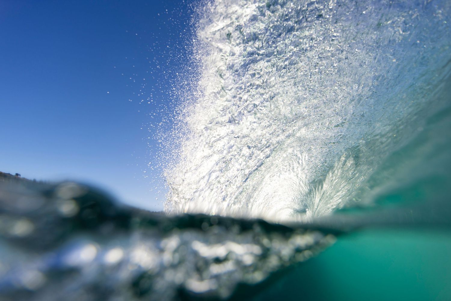 Breaking ocean wave creating a crystal clear underwater tunnel in turquoise waters.