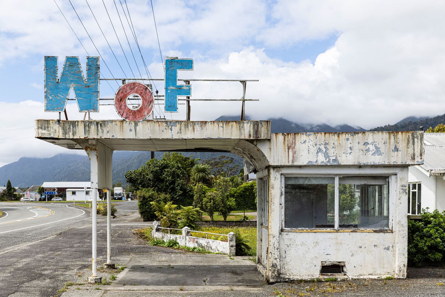 Abandoned commercial buildings with faded blue signage and power lines against cloudy sky.