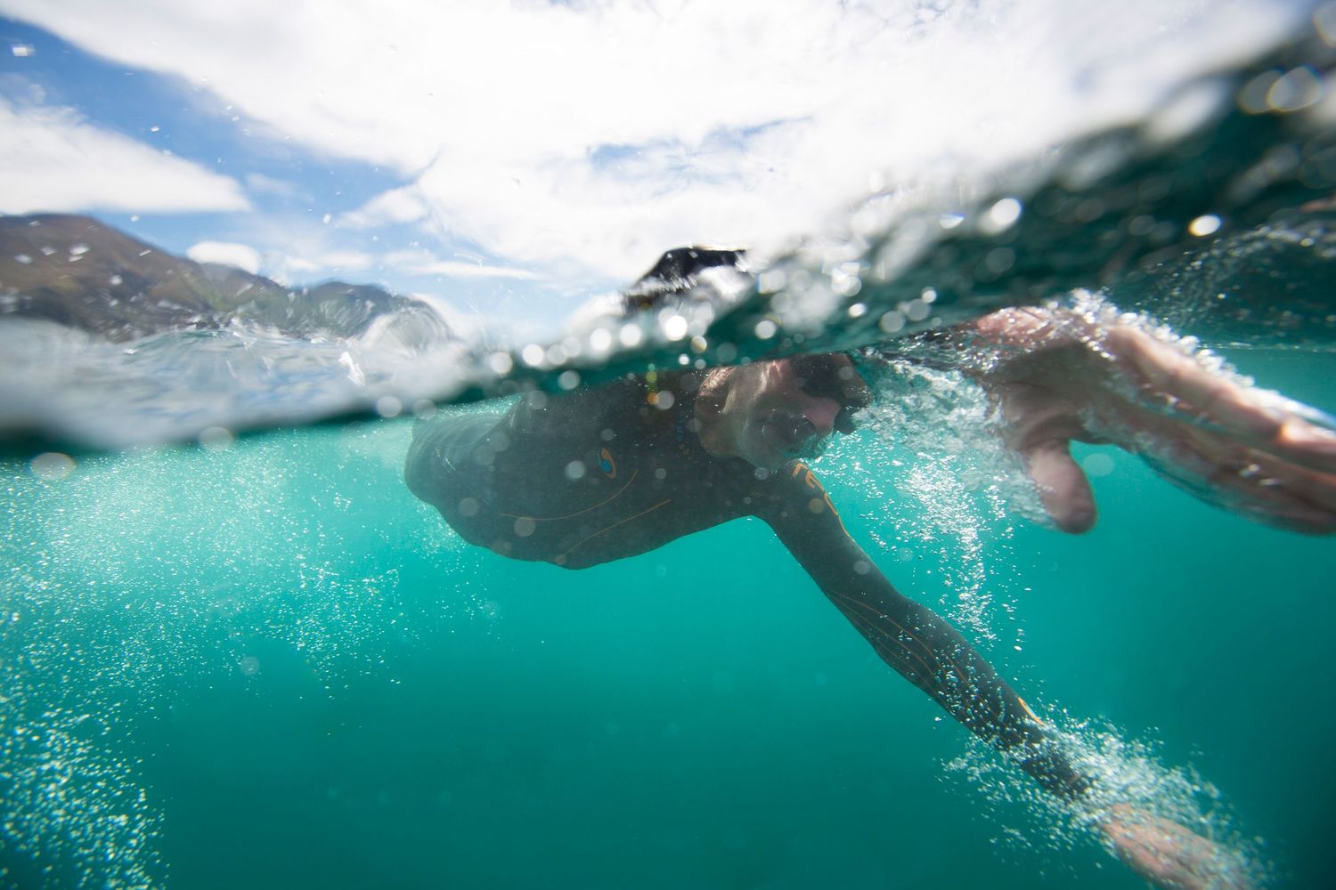 Underwater view of swimmer gliding through turquoise waters creating ripples and bubbles.