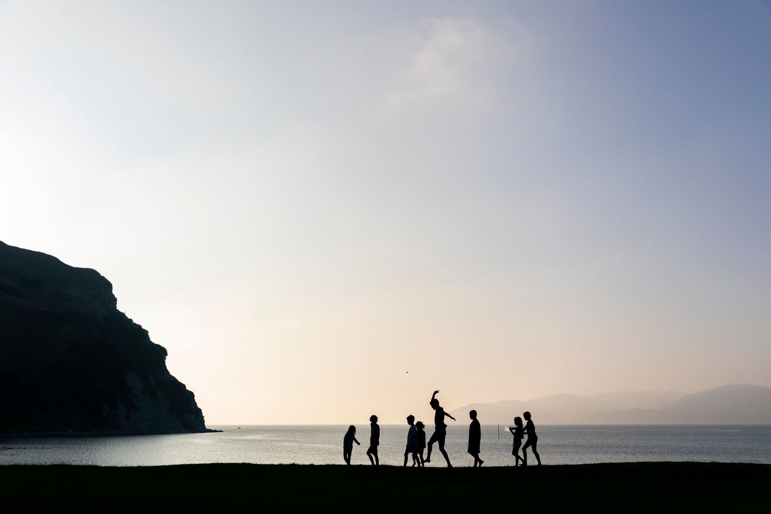 Silhouetted figures walk along a scenic coastal ridge against a dramatic sunset sky.