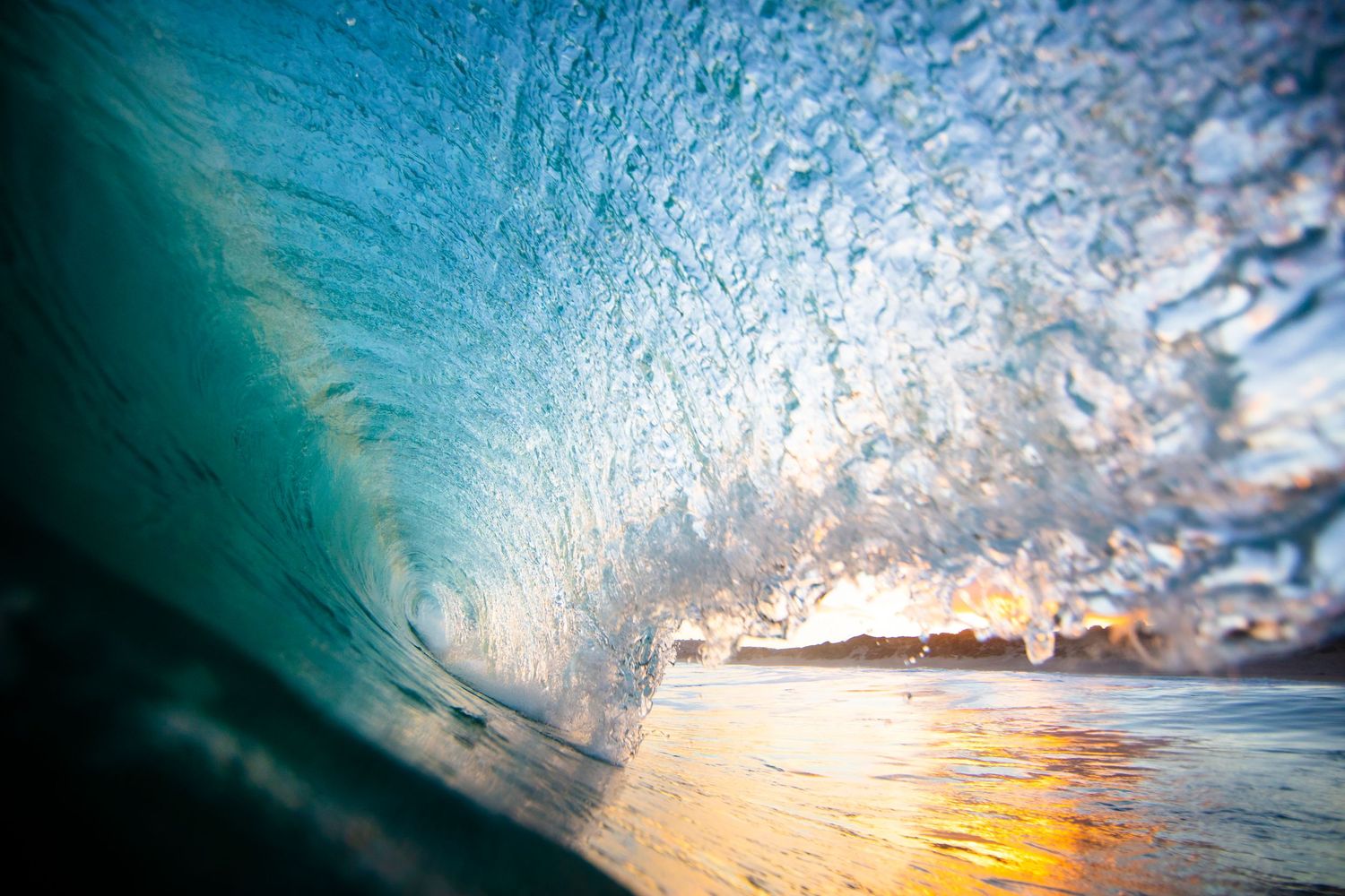 Inside view of a curling turquoise wave with sunlight streaming through the water.