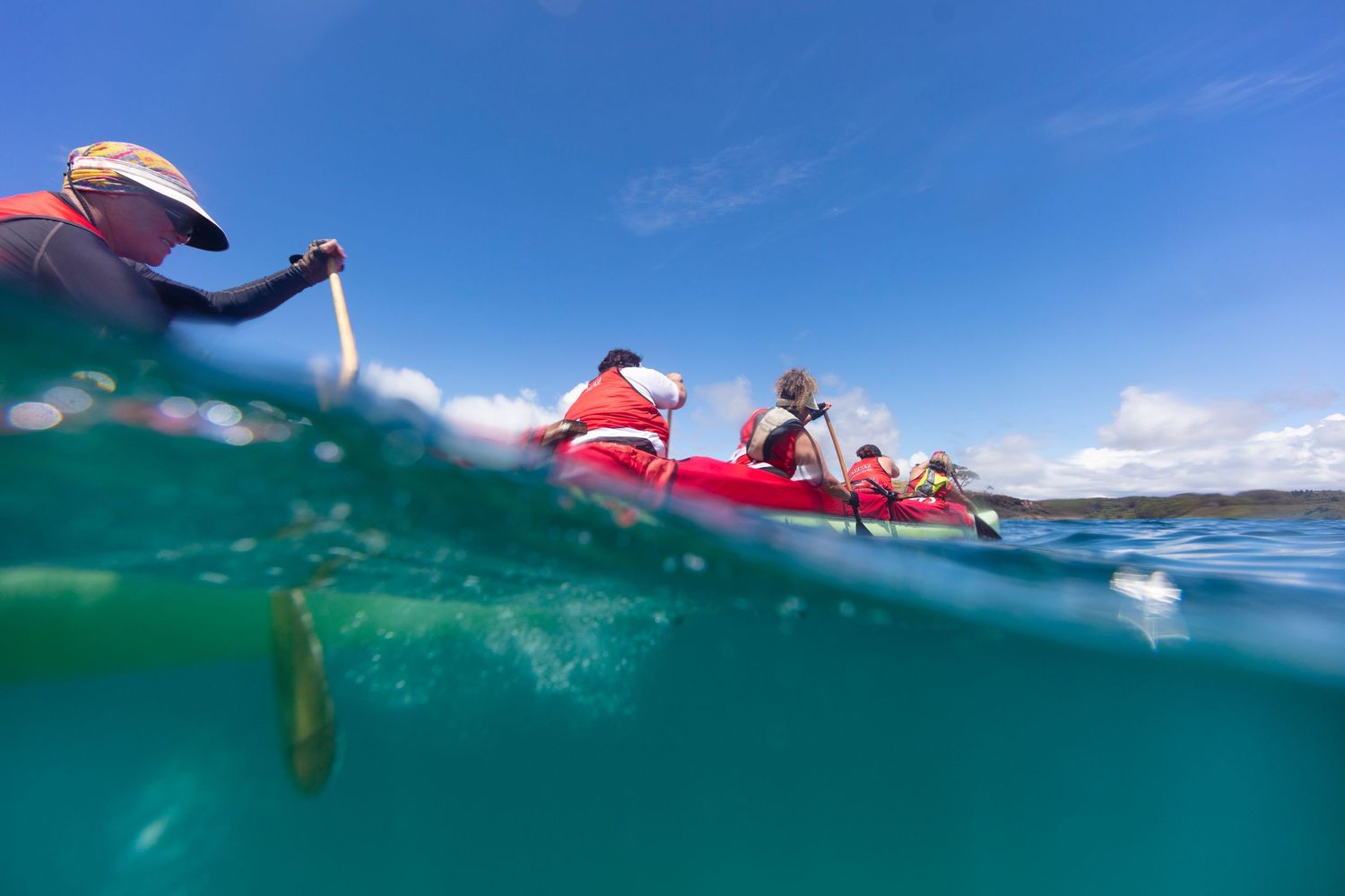 Split-shot photograph of waka ama paddlers in clear blue ocean waters.