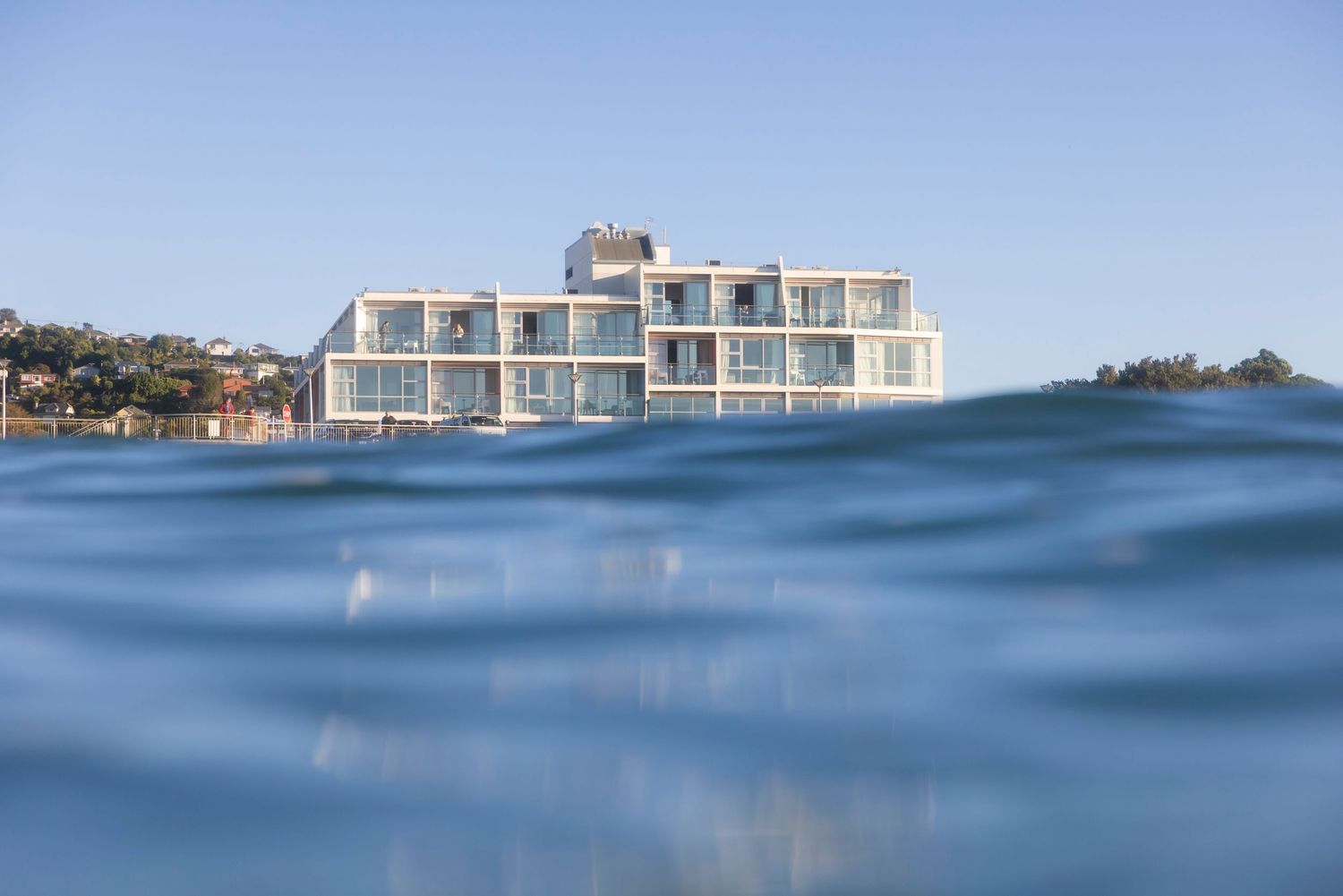 Low angle view of ocean waves with modern beachfront buildings visible in the distance.