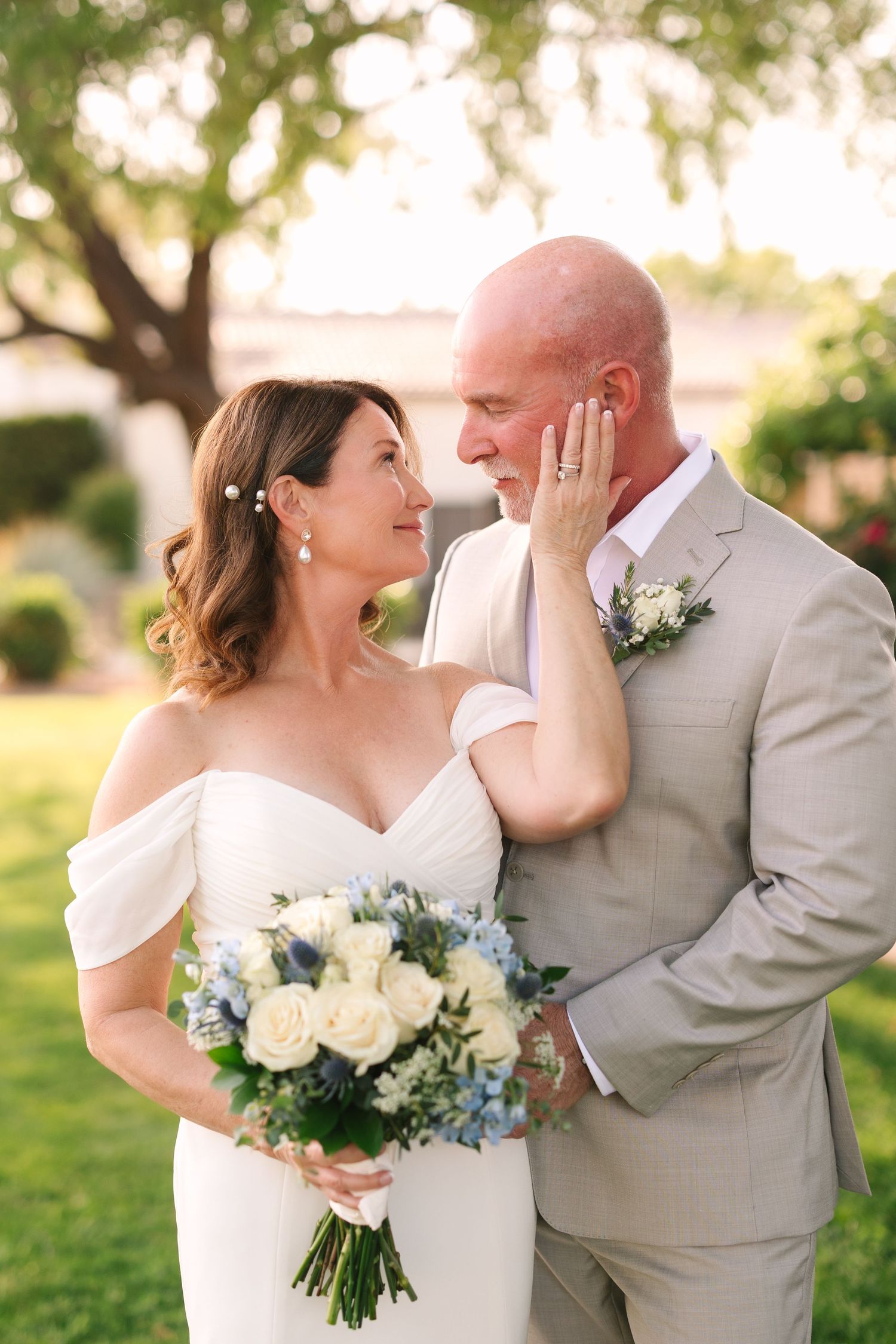 Romantic outdoor wedding photo series showing a couple embracing while holding a white and blue floral bouquet at sunset.