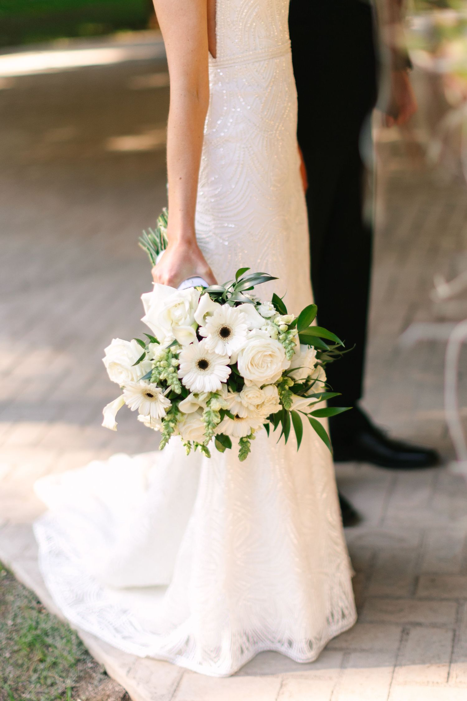 White wedding bouquet with gerbera daisies and roses against a bridal gown.