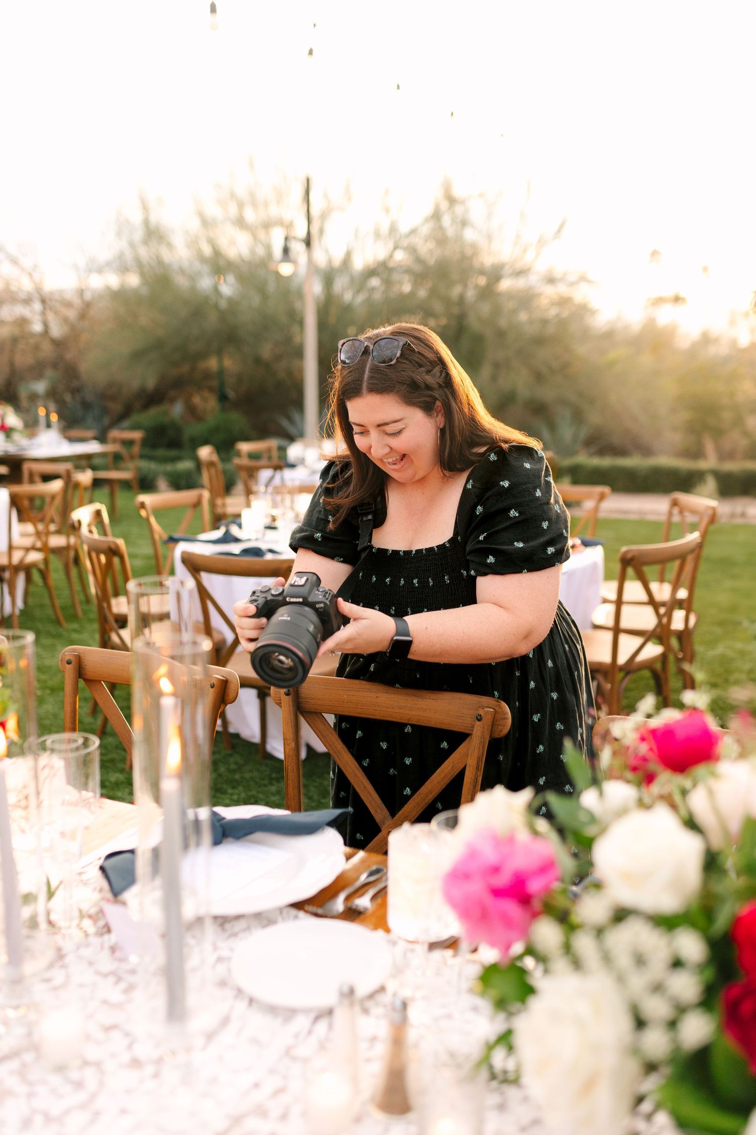 Photographer reviewing images on camera at elegant outdoor table setting with floral centerpiece at sunset. Molly McPhoto