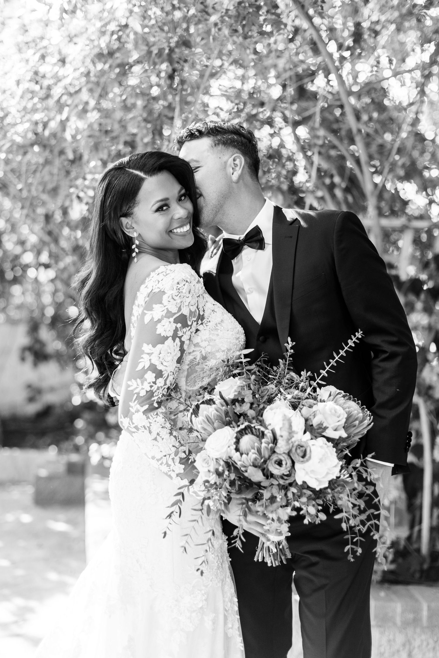 A romantic black and white wedding photo capturing a couple sharing an intimate moment with a beautiful floral bouquet.