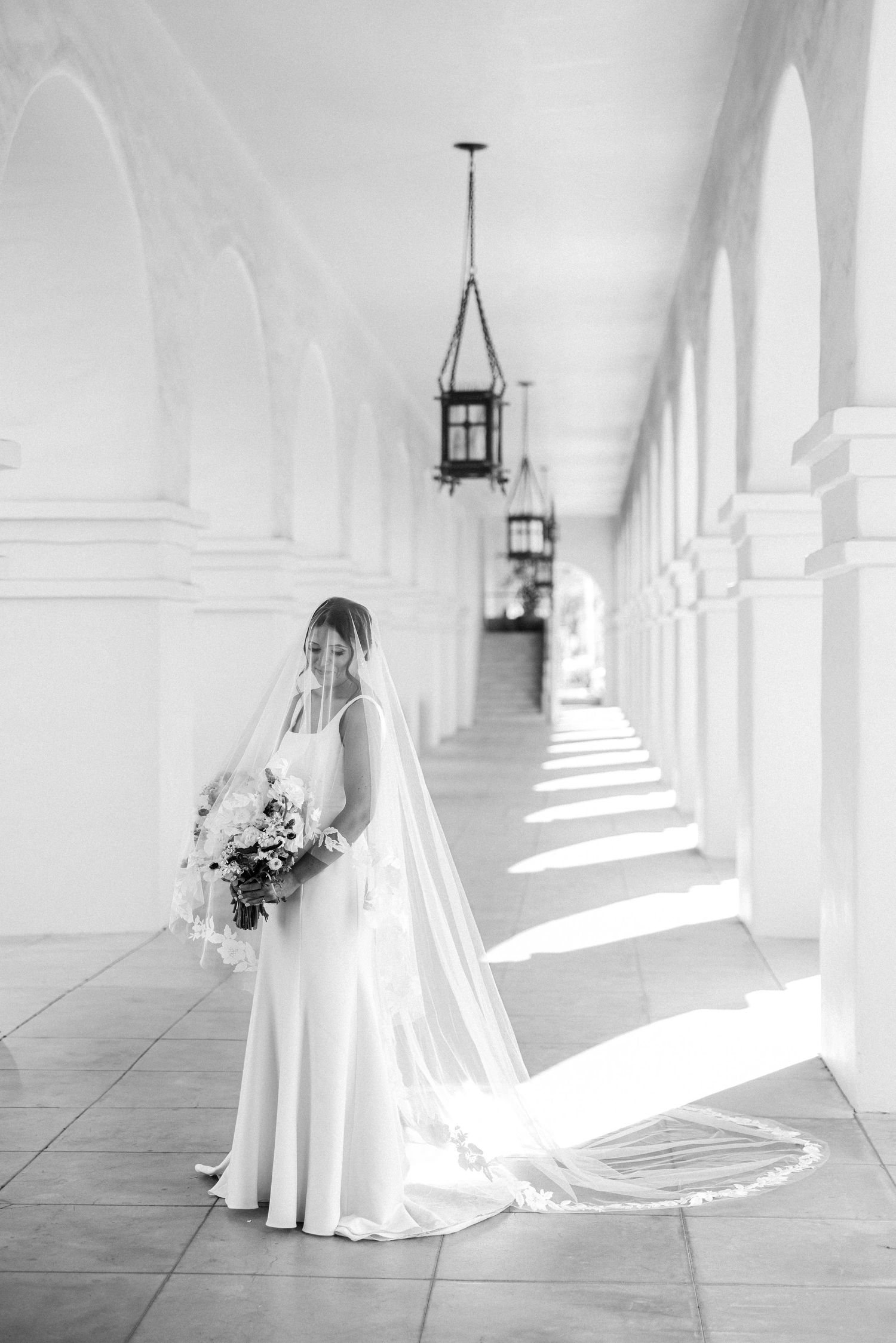 Black and white series of a bride in a flowing white dress and veil walking through a sunlit colonnade hallway.