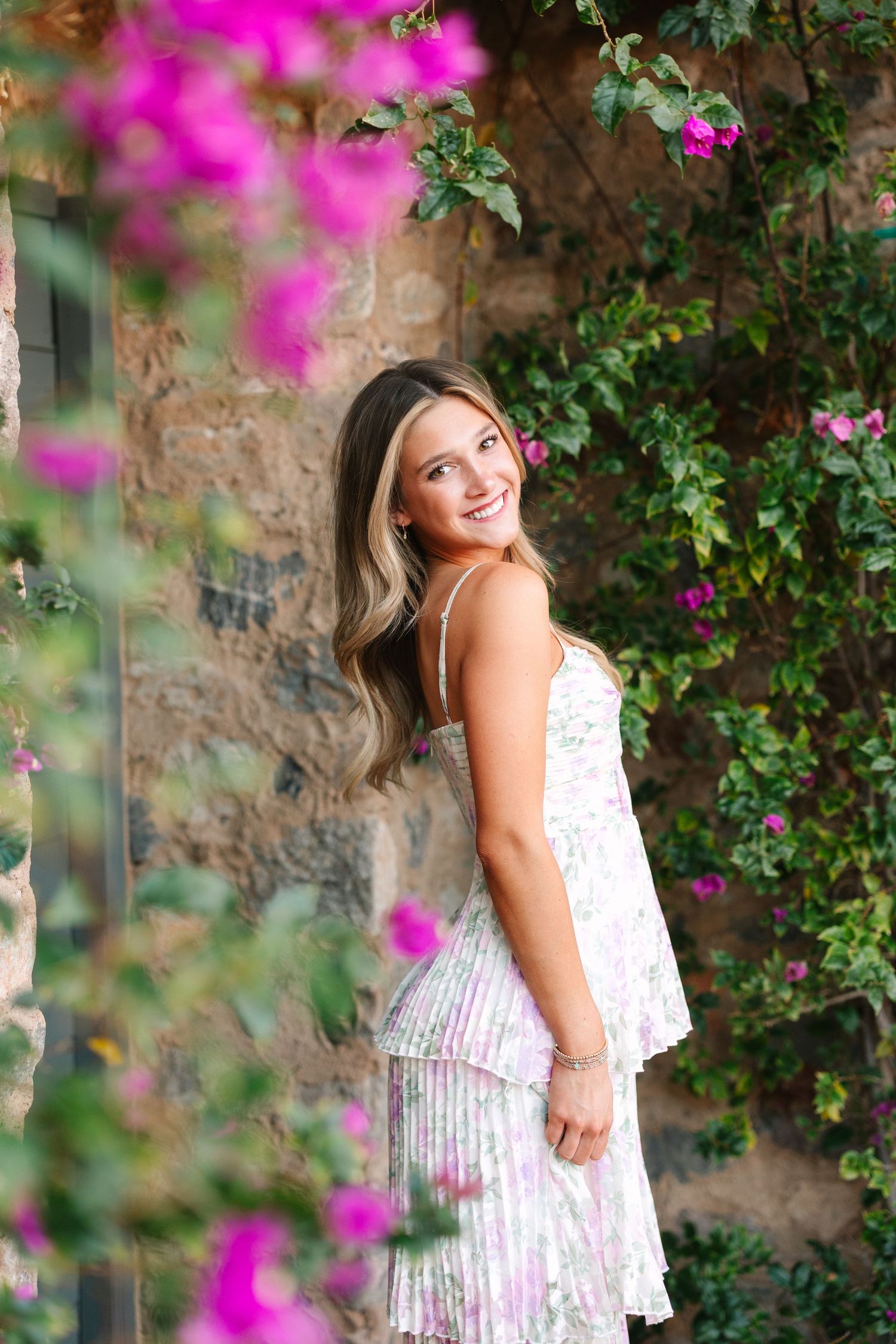 Outdoor portrait against rustic stone wall with vibrant pink bougainvillea flowers creating a romantic garden setting.