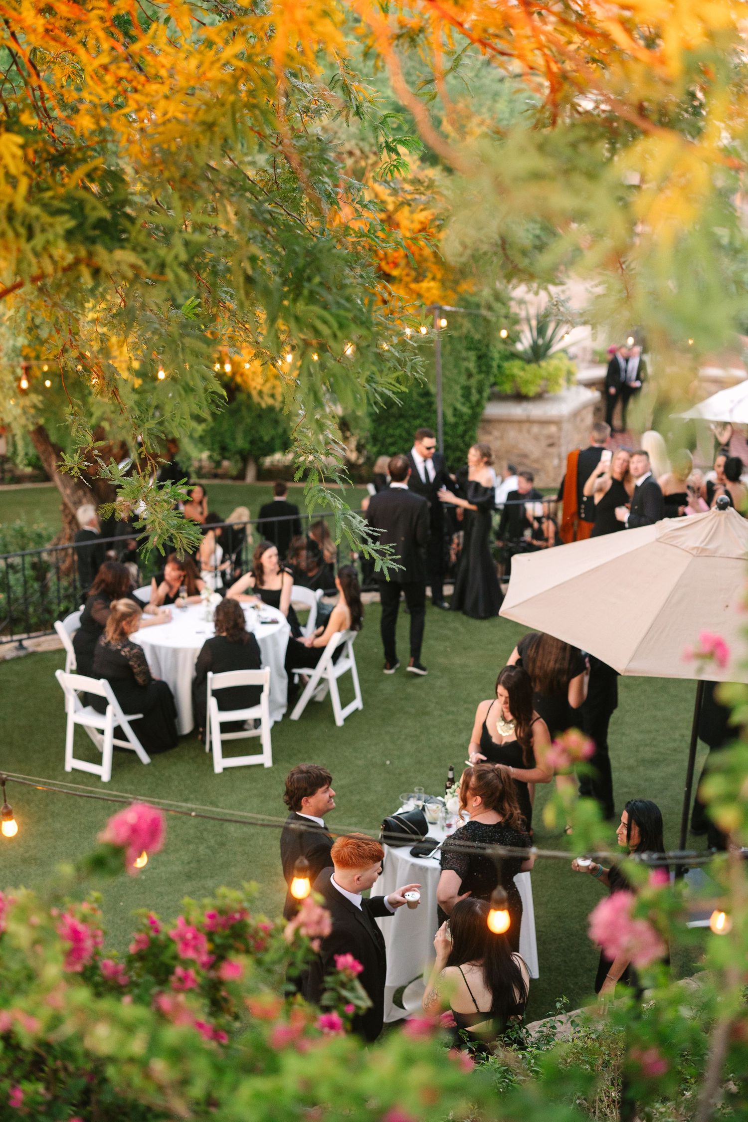 An outdoor garden wedding reception with guests seated at tables under autumn trees.