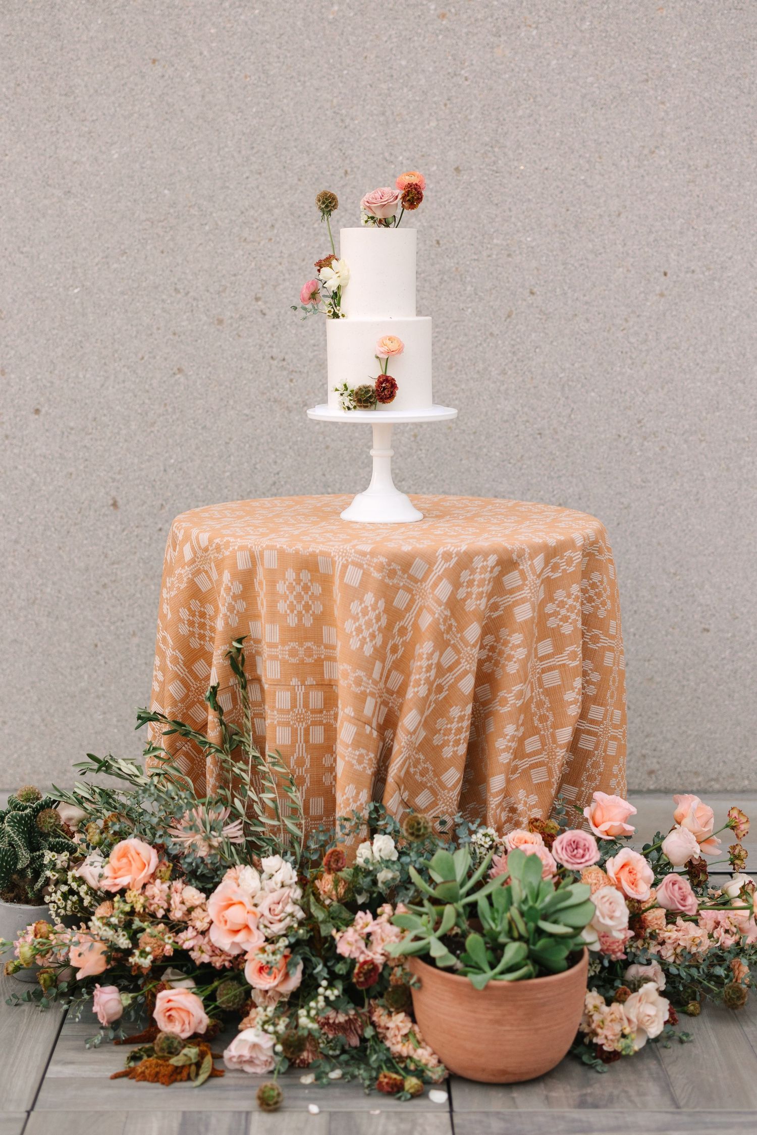 An elegant wedding cake display with peach linens and succulent florals.