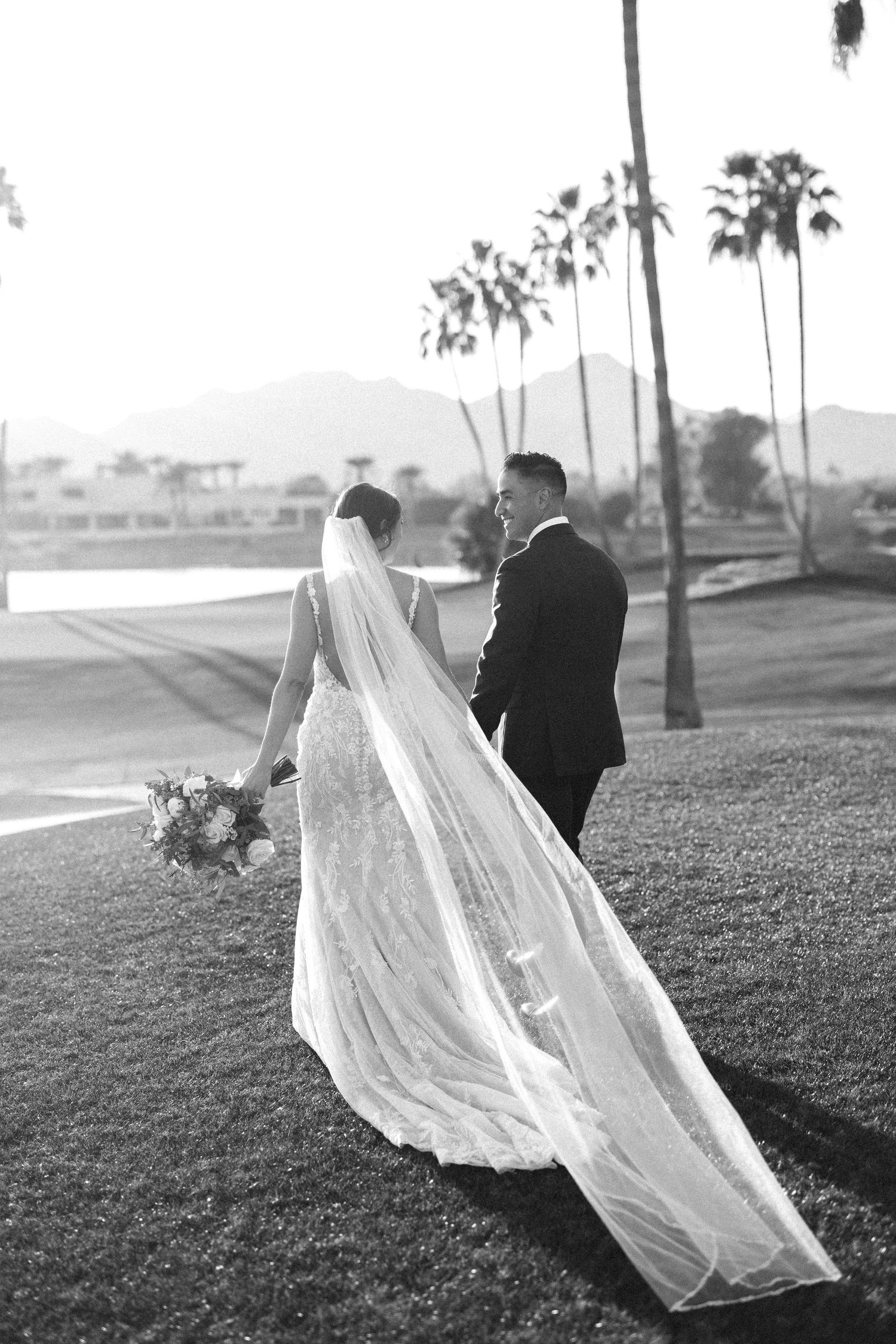 Black and white wedding photo with palm trees and mountains in background.