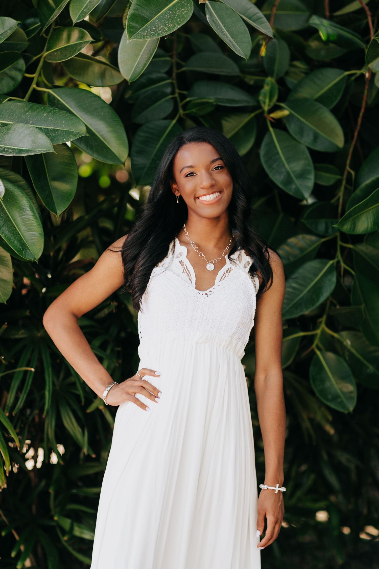 A summery white sleeveless dress is showcased in a garden photoshoot against lush green foliage background.