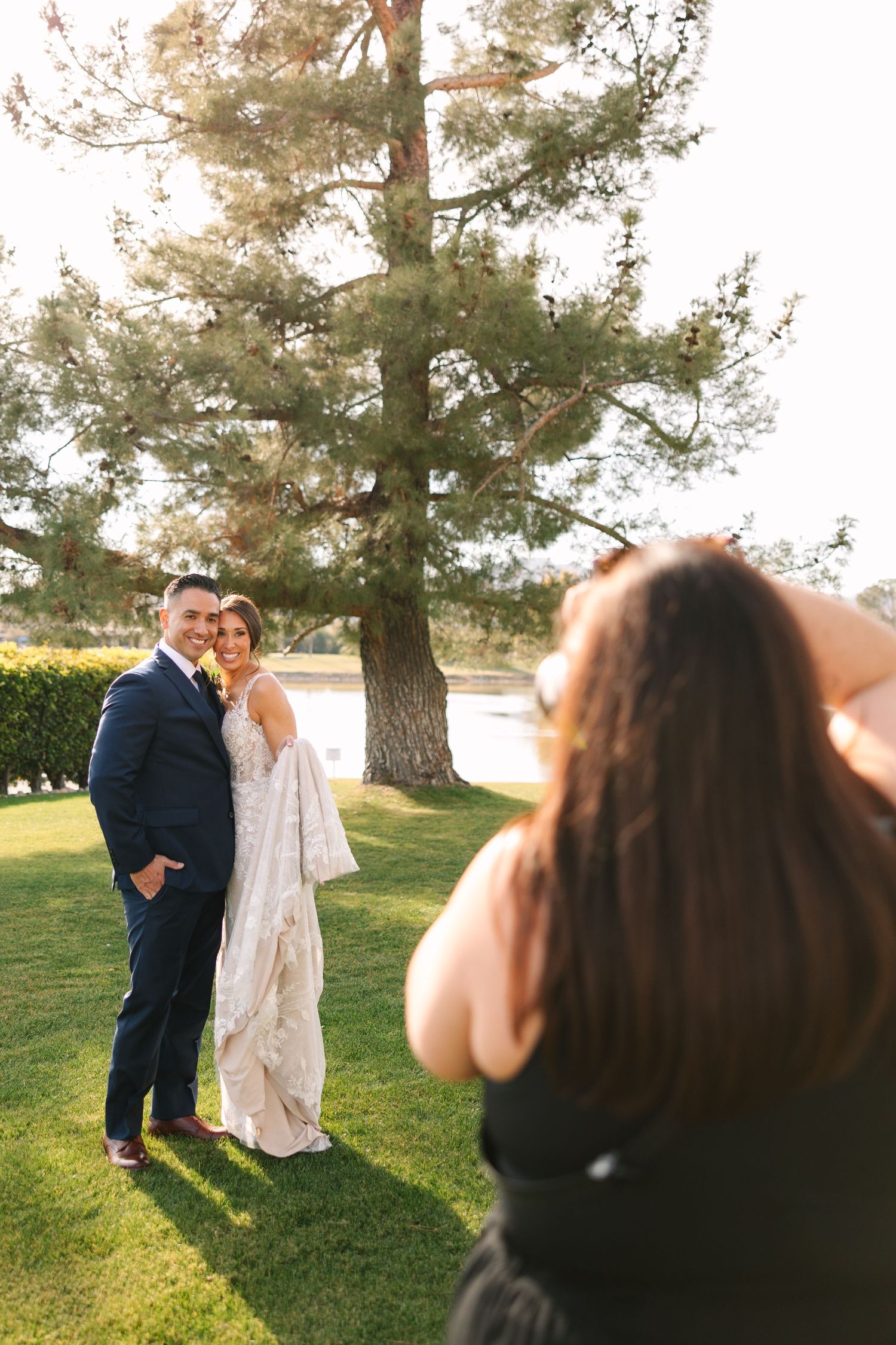 Behind-the-scenes shot of photographer capturing couple's wedding portraits under tall pine tree. McCormick Ranch Golf Club Scottsdale AZ