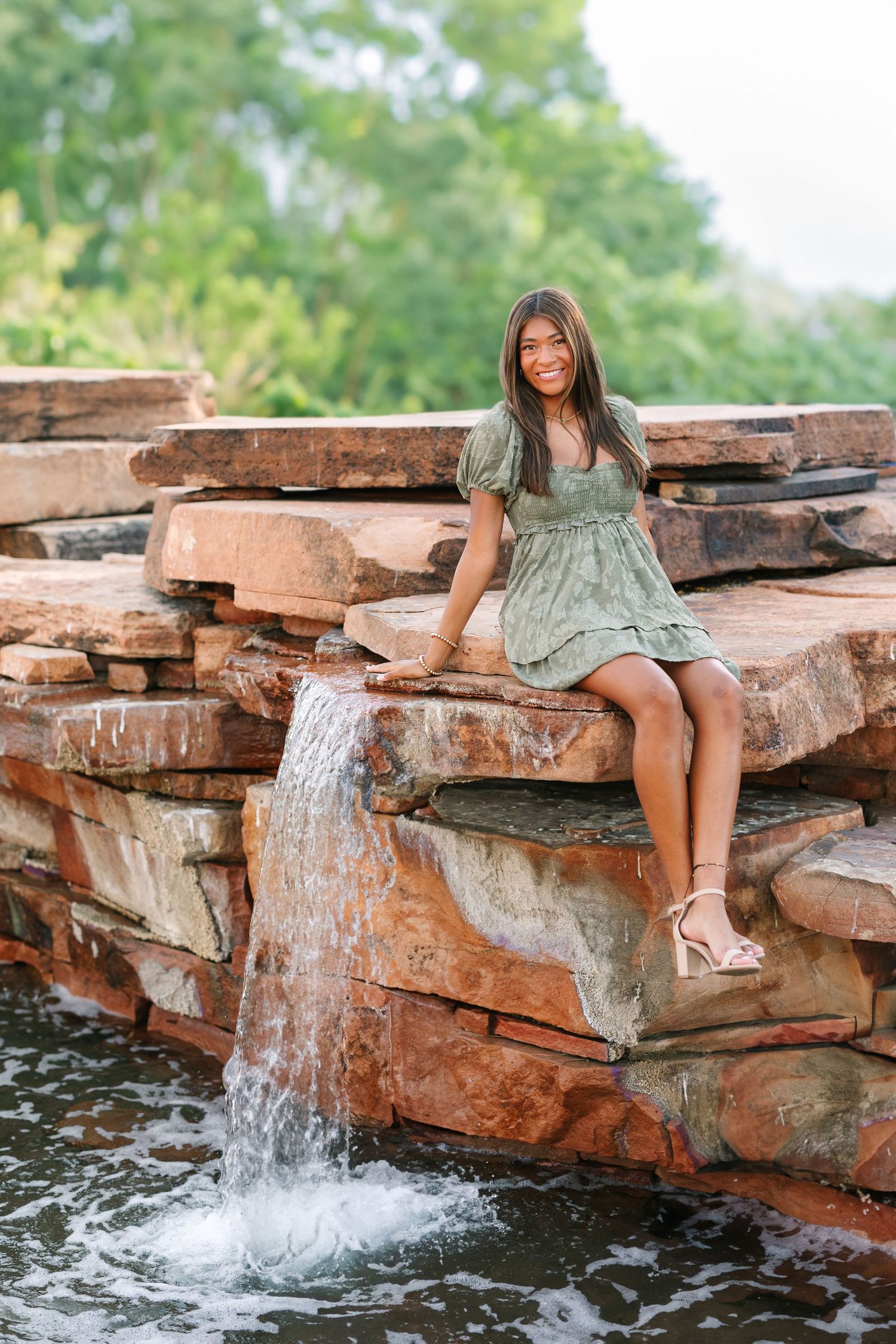 A mint green dress and sandals complement a rustic waterfall scene with layered stone ledges in a natural outdoor setting.