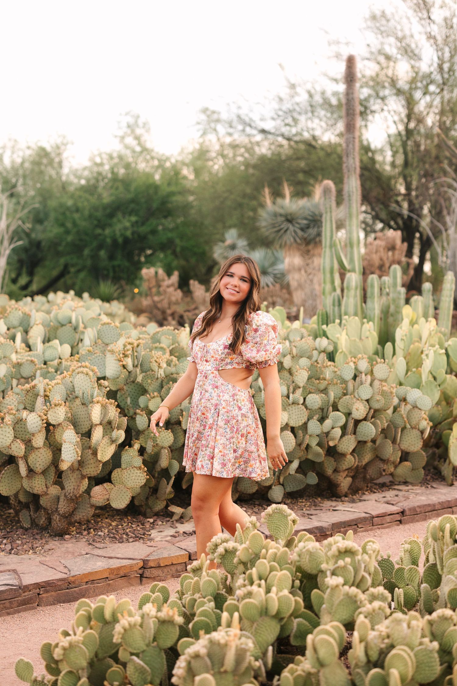 A floral dress stands out against a backdrop of prickly pear cactus in a desert garden setting.