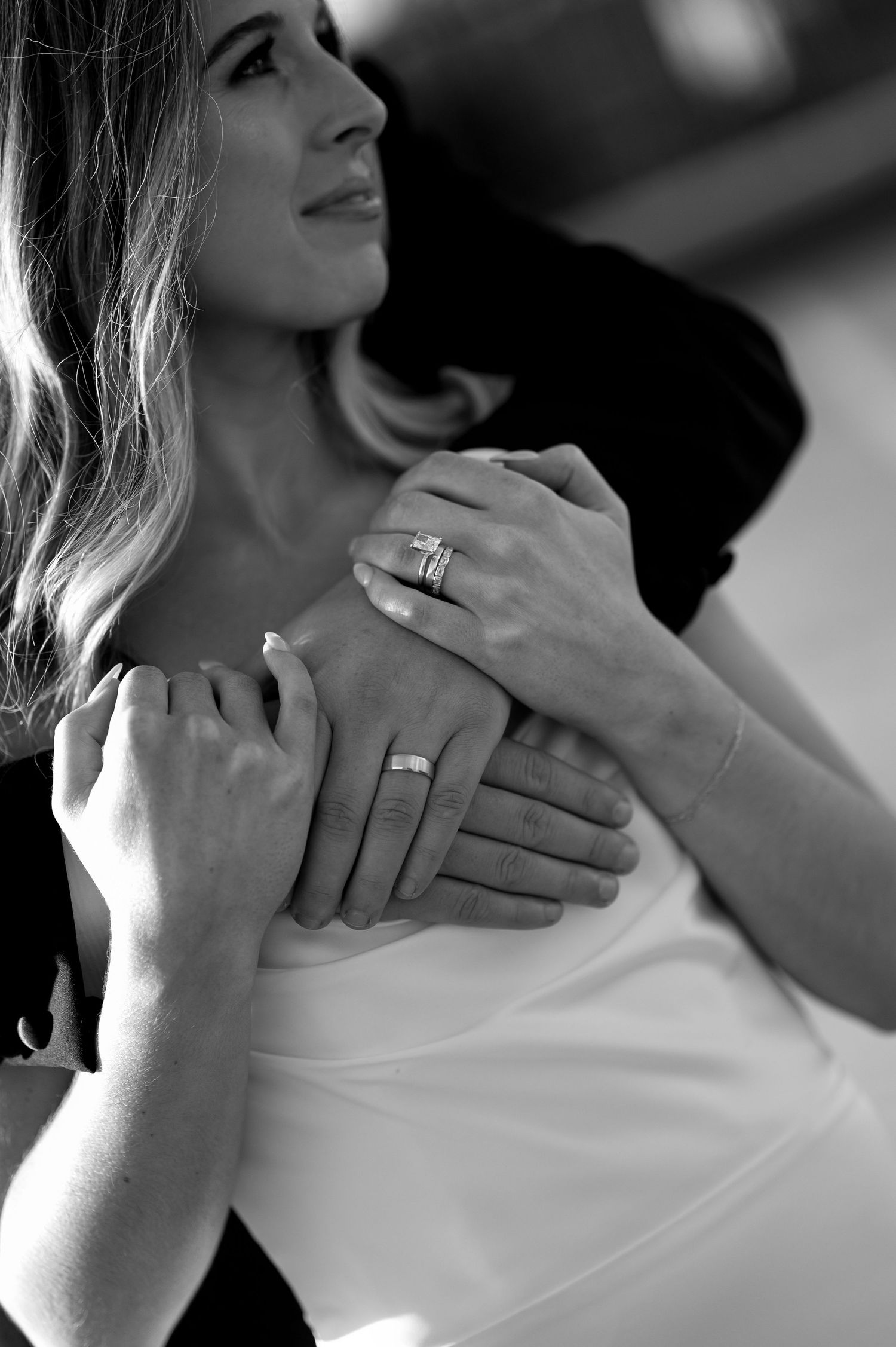 Black and white photo showing hands with wedding rings touching in an intimate romantic moment.