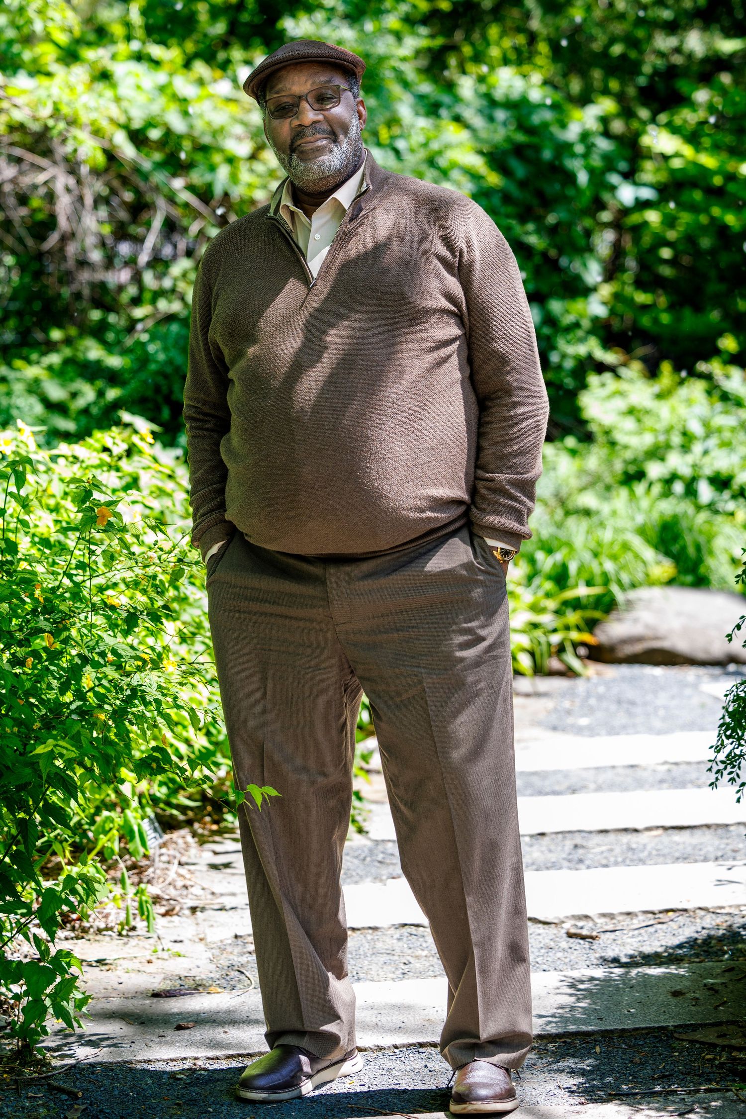 Casual portrait of senior man in brown sweater standing on garden path.