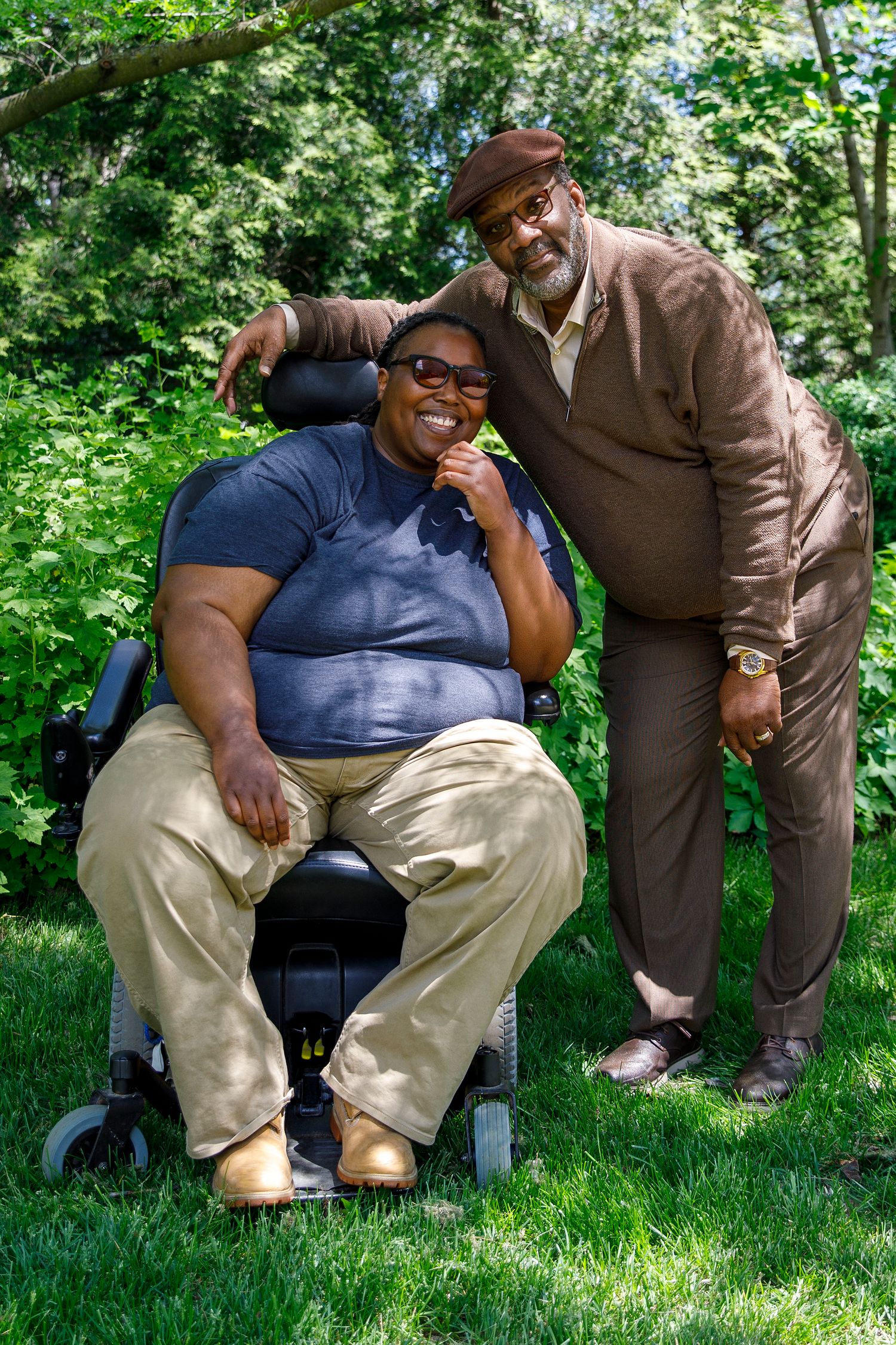 Two people sharing a warm moment outdoors on a sunny day with lush green foliage in the background.