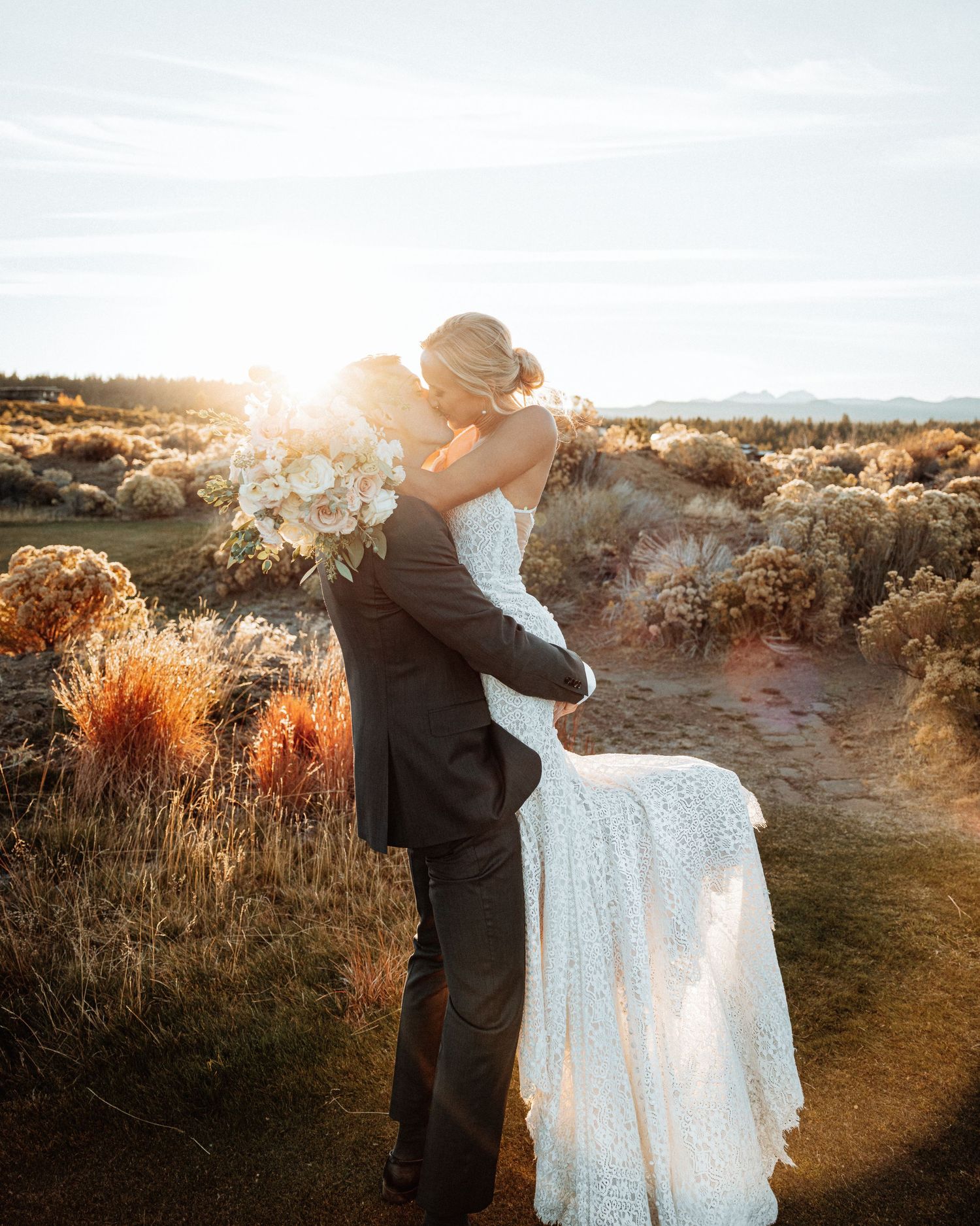 A groom lifts his new wife as they kiss. The sun set behind them in Bellingham WA.