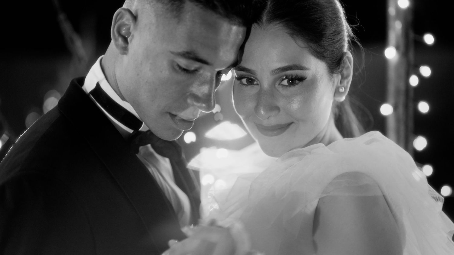 Romantic black and white wedding portrait of a couple in elegant formal attire sharing an intimate moment.