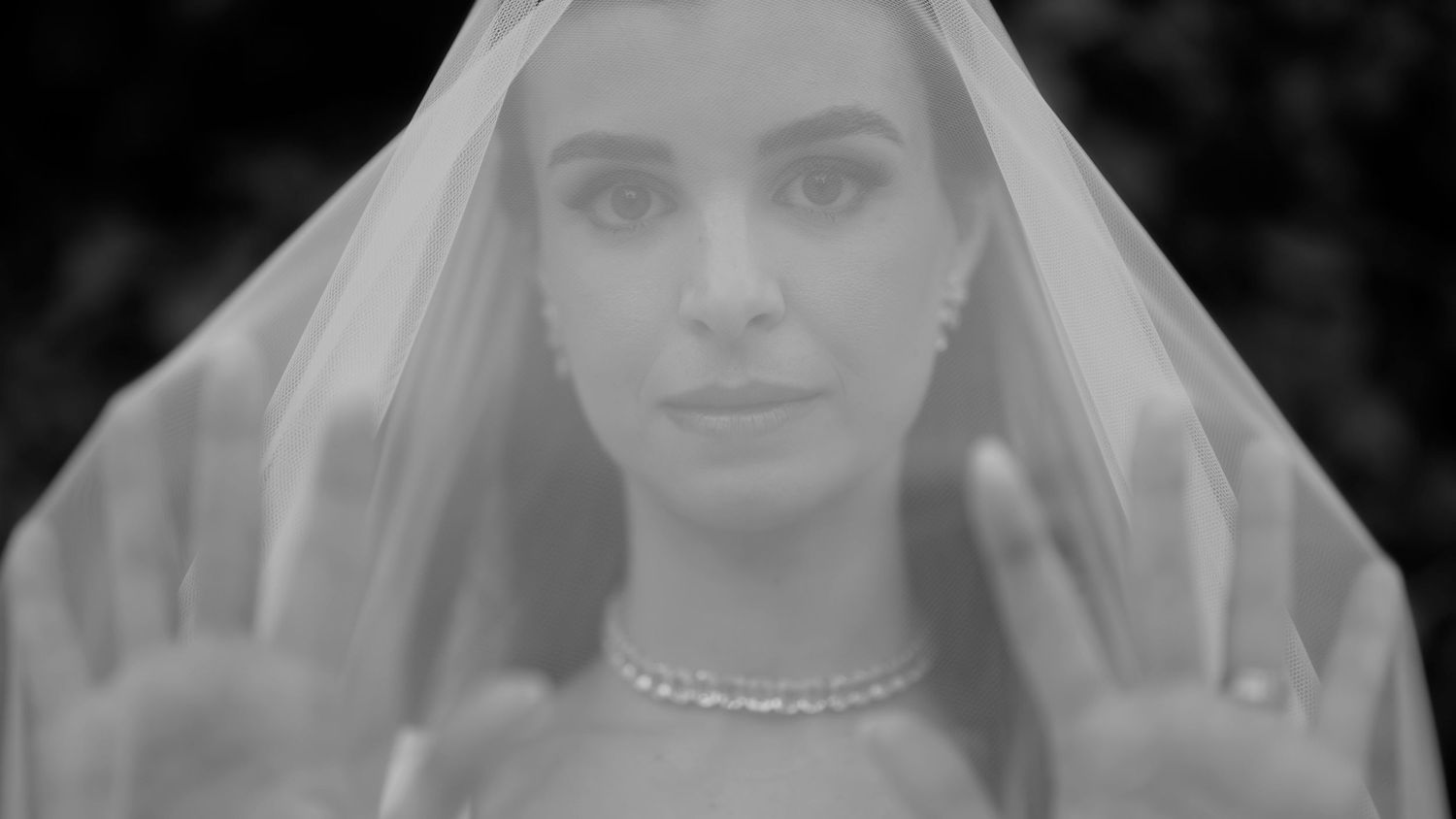 A bride in a white veil and delicate necklace poses for an ethereal black and white portrait.