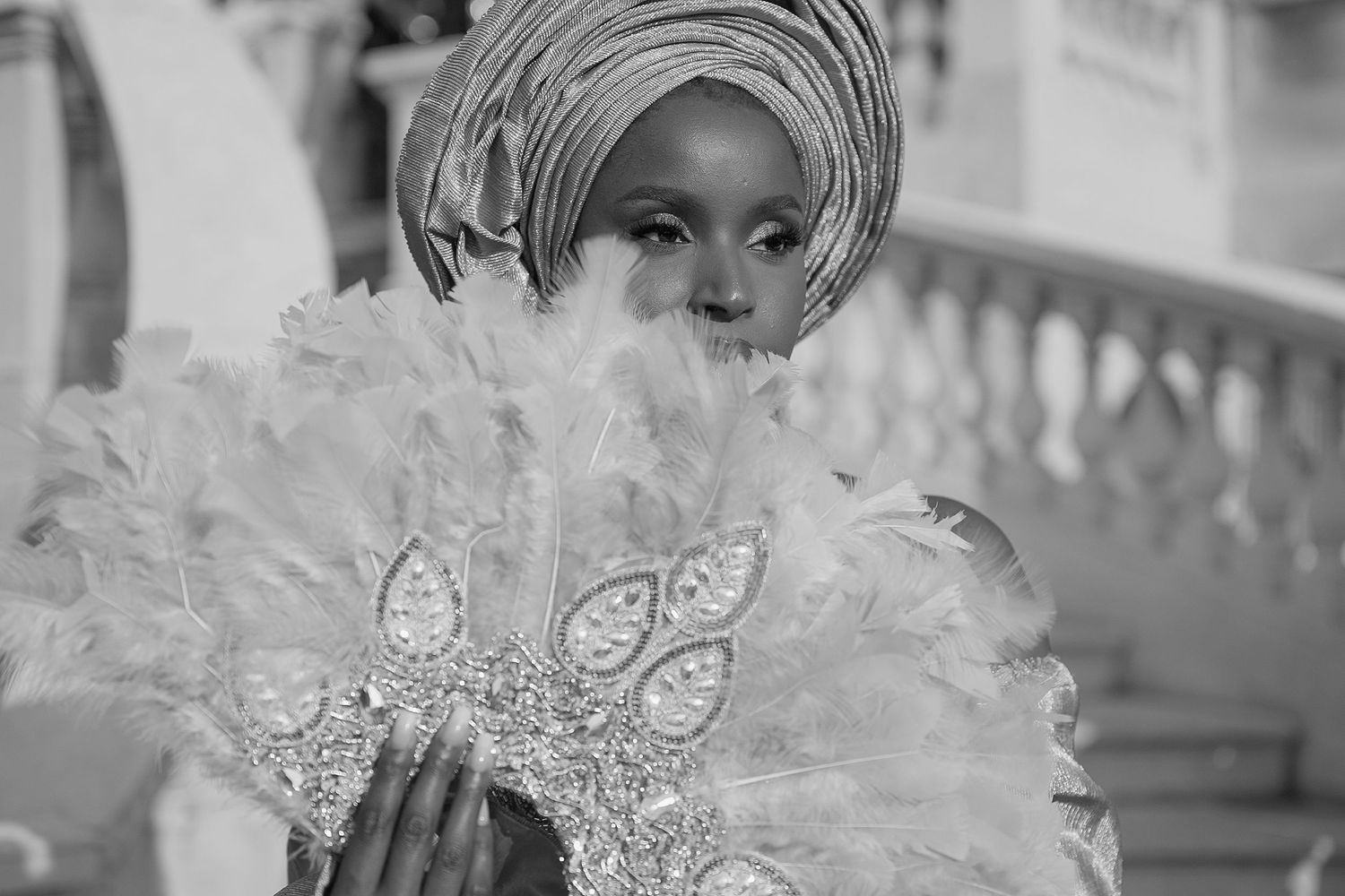 A black and white photograph capturing someone wearing traditional Nigerian attire with an ornate gele headpiece and lace details.