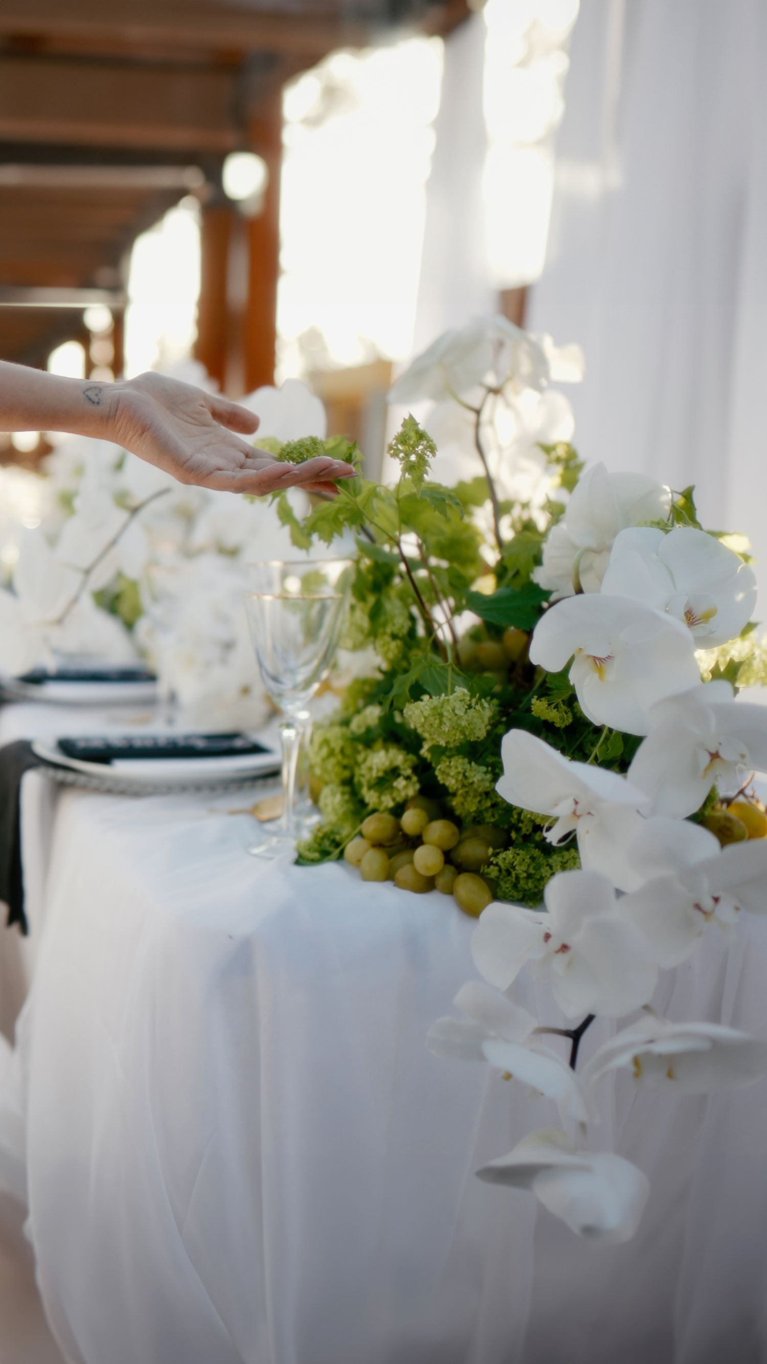 Elegant table setting with white orchids, green grapes, and floral arrangements on a crisp white tablecloth at a formal event.