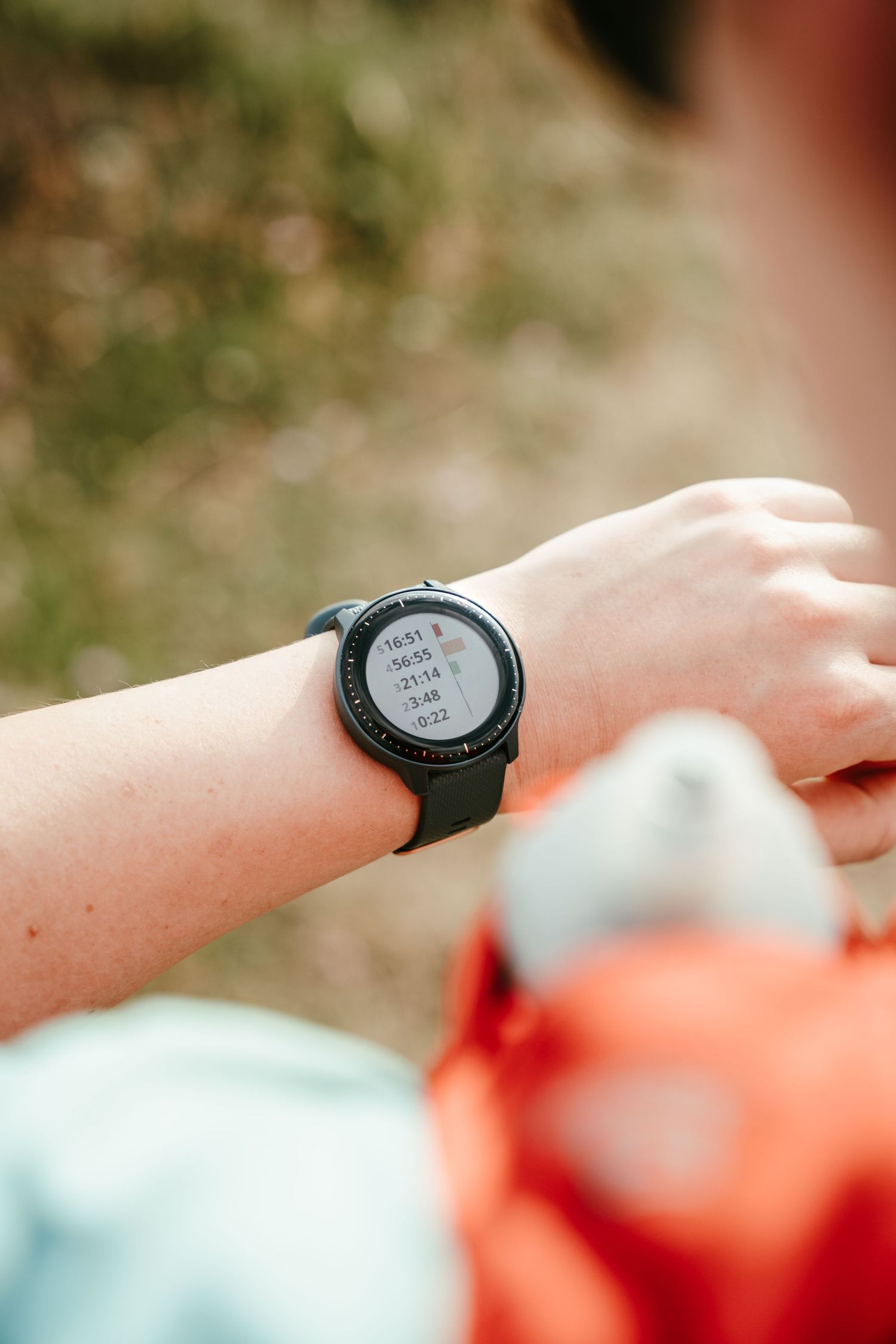 A smartwatch displaying digital time reading on someone's wrist against a blurred outdoor background.