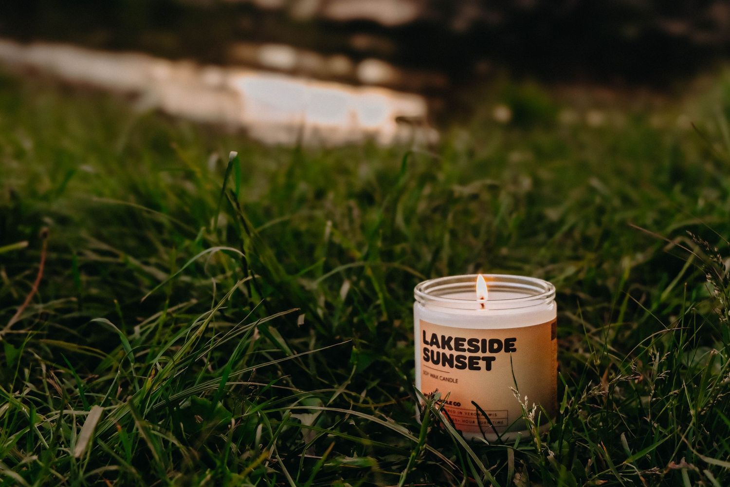 A product photo of a candle lit in the grass by the lake taken by Life Well Spent Photography
