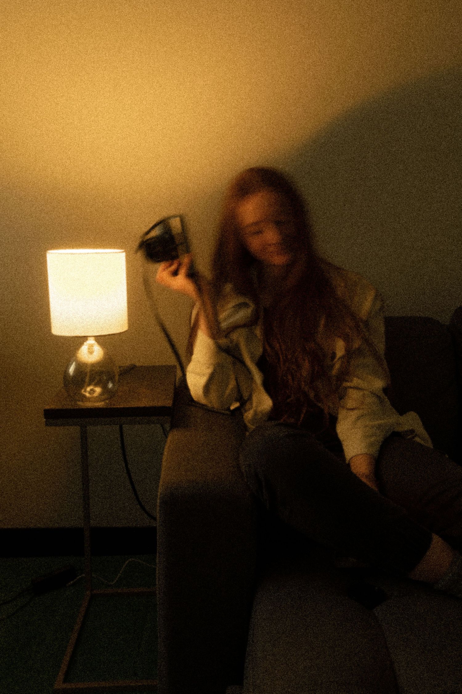 Photographer sits on couch in dimly lit room with table lamp creating warm ambient lighting.
