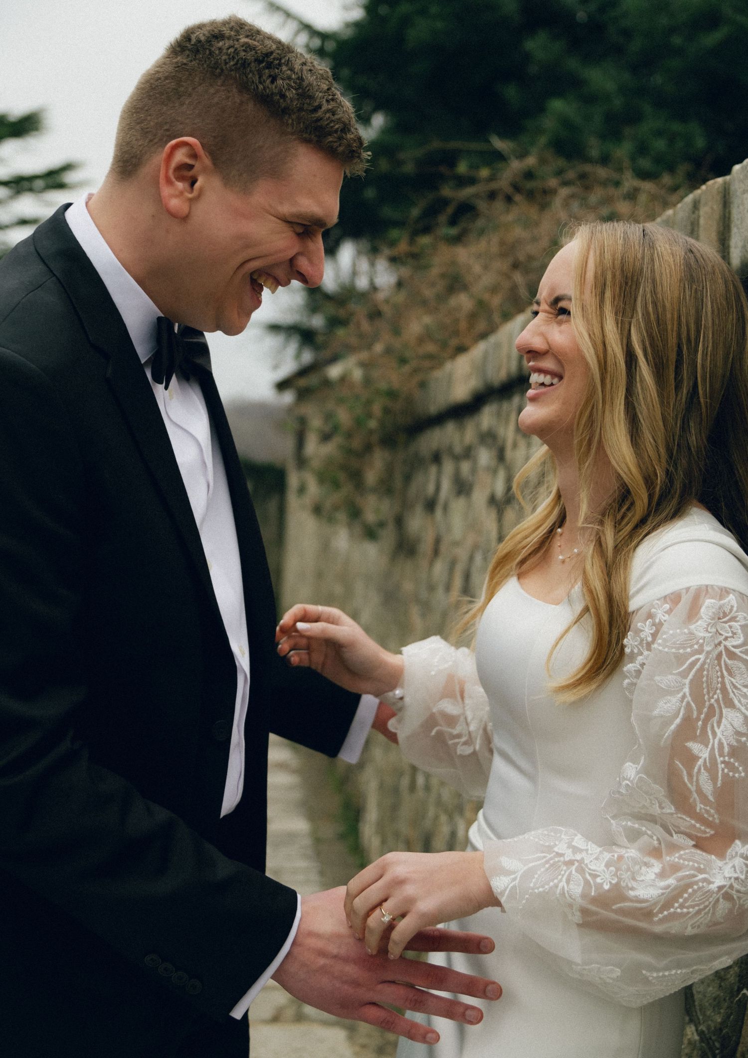 A joyful couple shares a candid laughing moment together on their wedding day wearing formal attire.