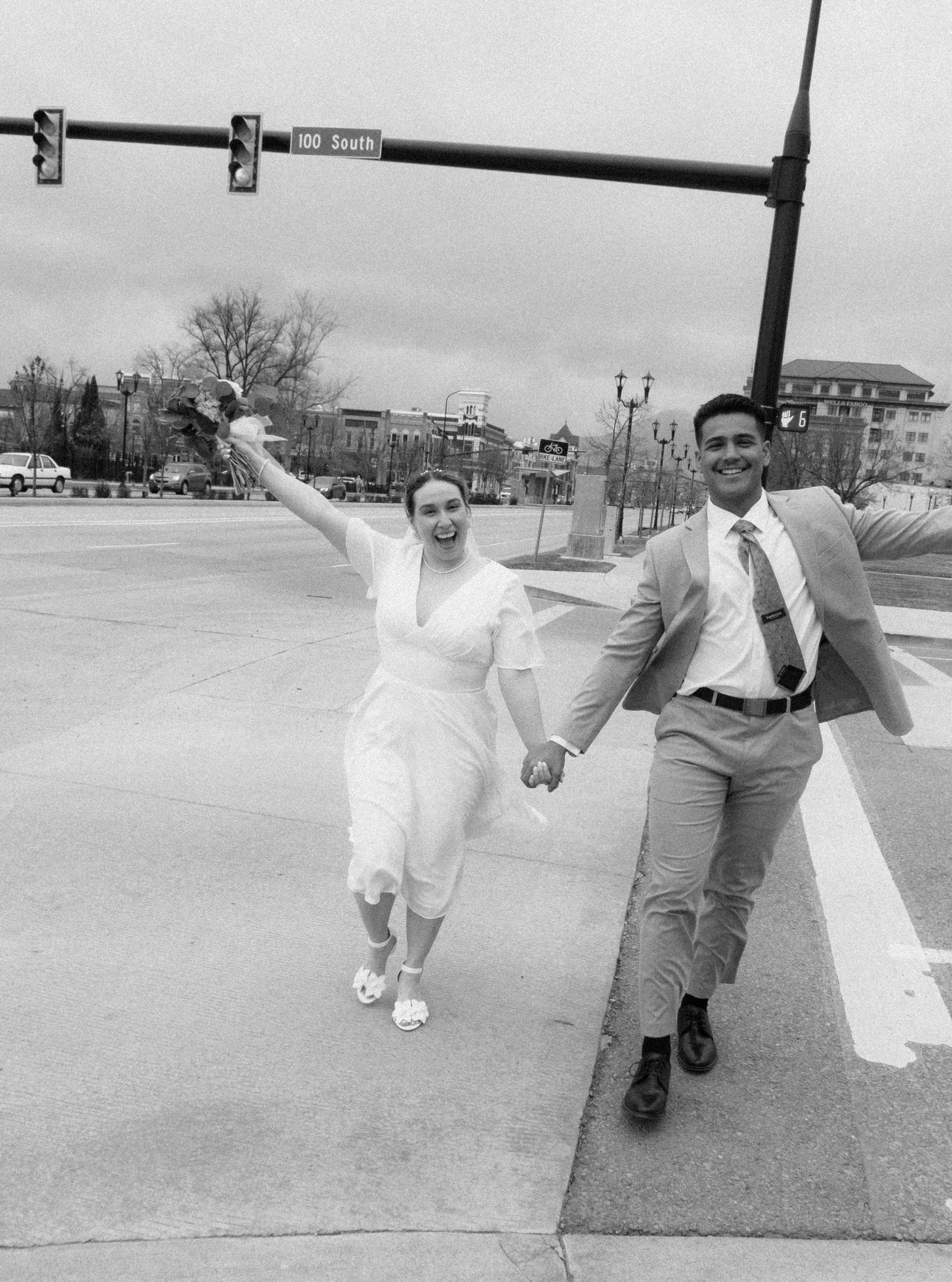A joyful couple running and holding hands on a city street in black and white photography.
