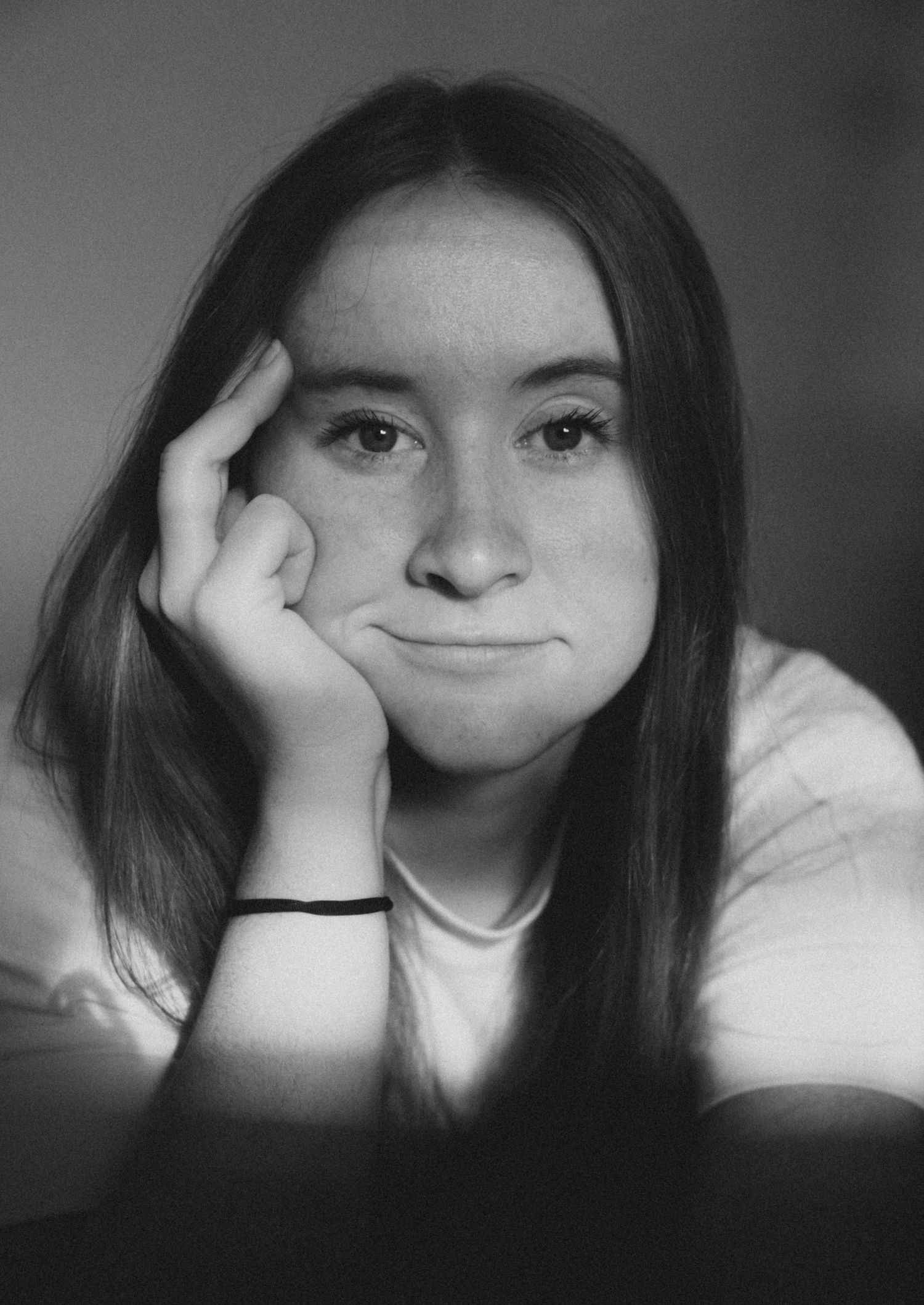A black and white portrait showing a young person resting their head on their hand with a slight smile.