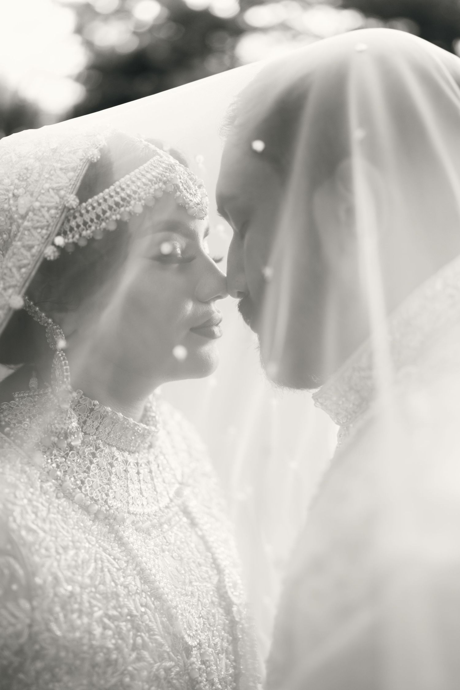 Romantic black and white wedding photo showing bride and groom in close intimate moment under delicate veils.