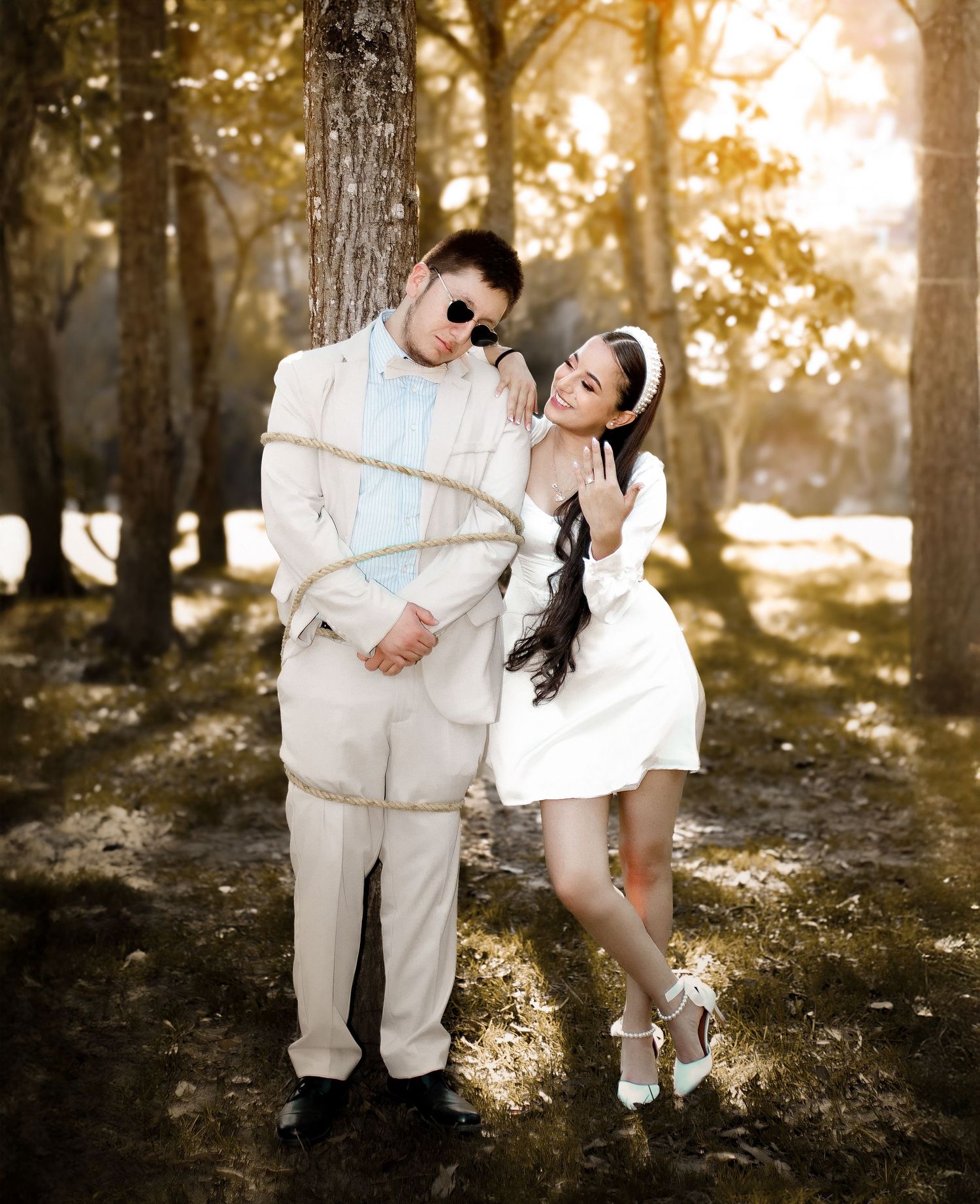 Couple in matching white outfits pose together in a dreamy forest setting with golden sunlight filtering through trees.