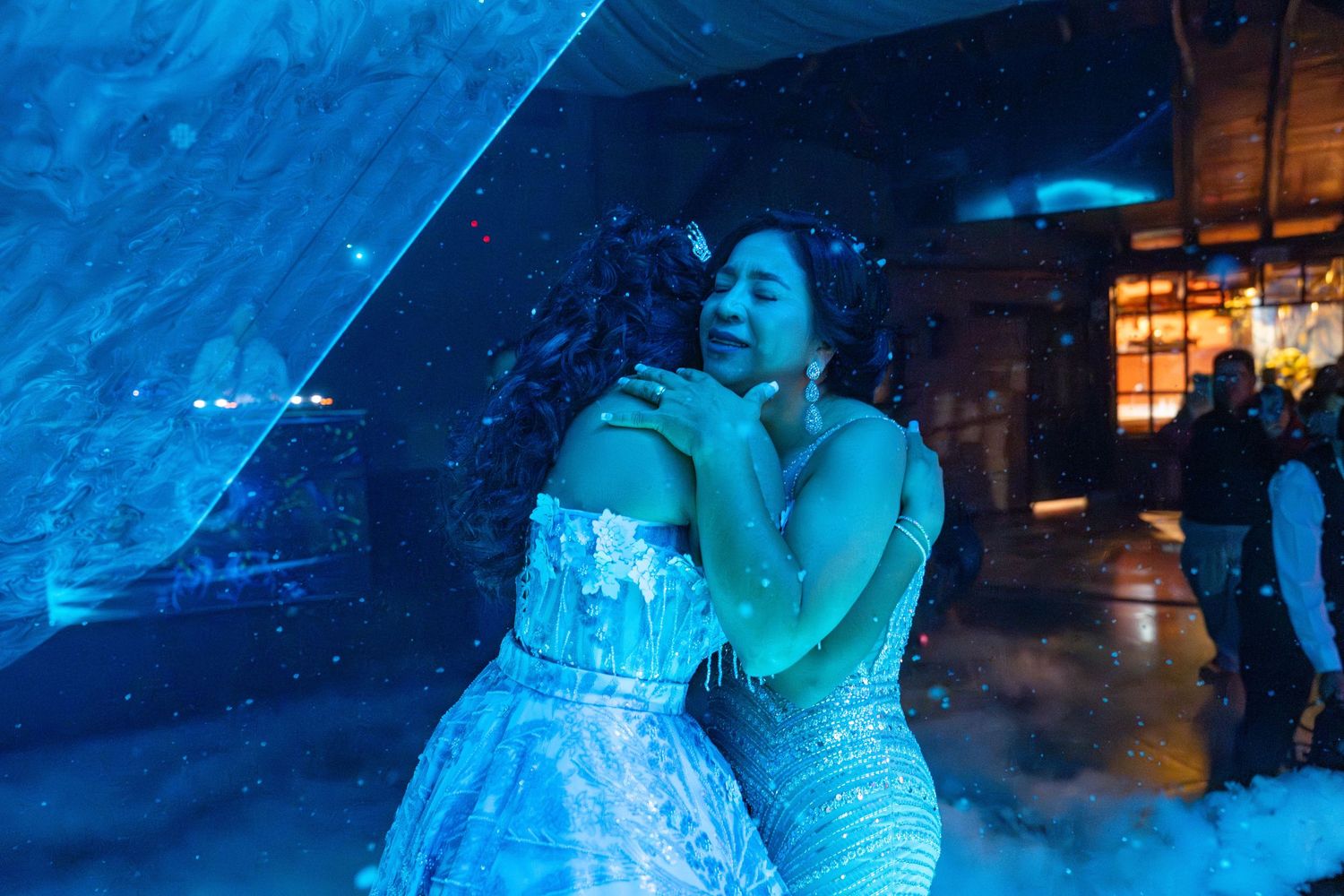 Two figures sharing an intimate dance moment bathed in ethereal blue lighting at what appears to be a wedding reception.