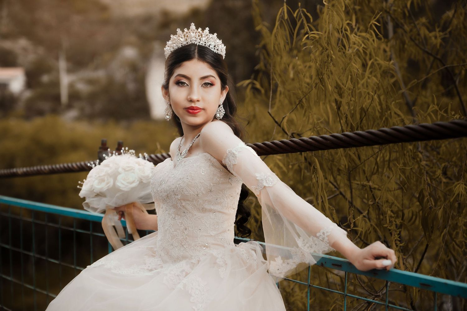 An elegant bride in a white ballgown and crown poses against a nature backdrop.