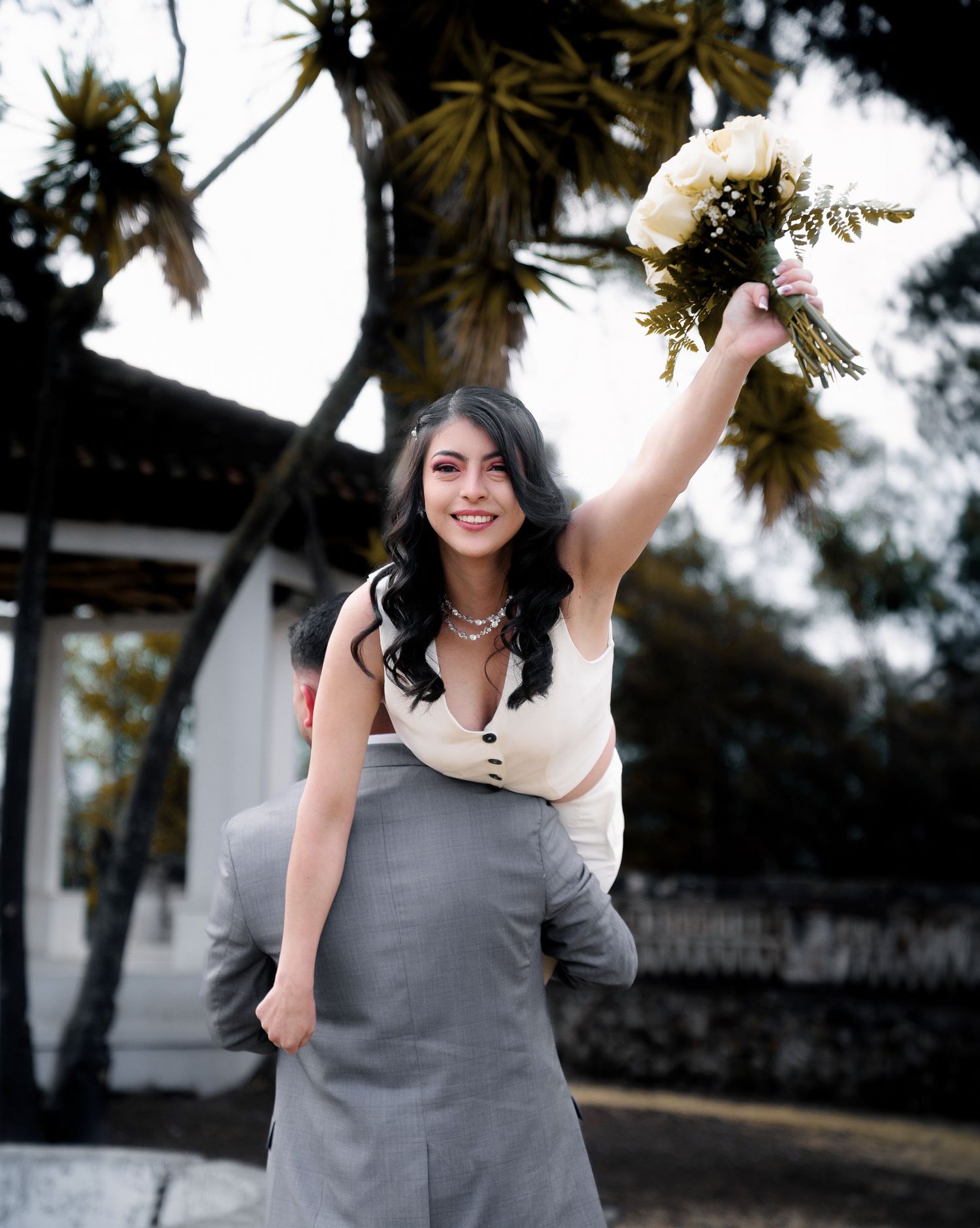 Person in grey dress holds white bouquet against tropical background.