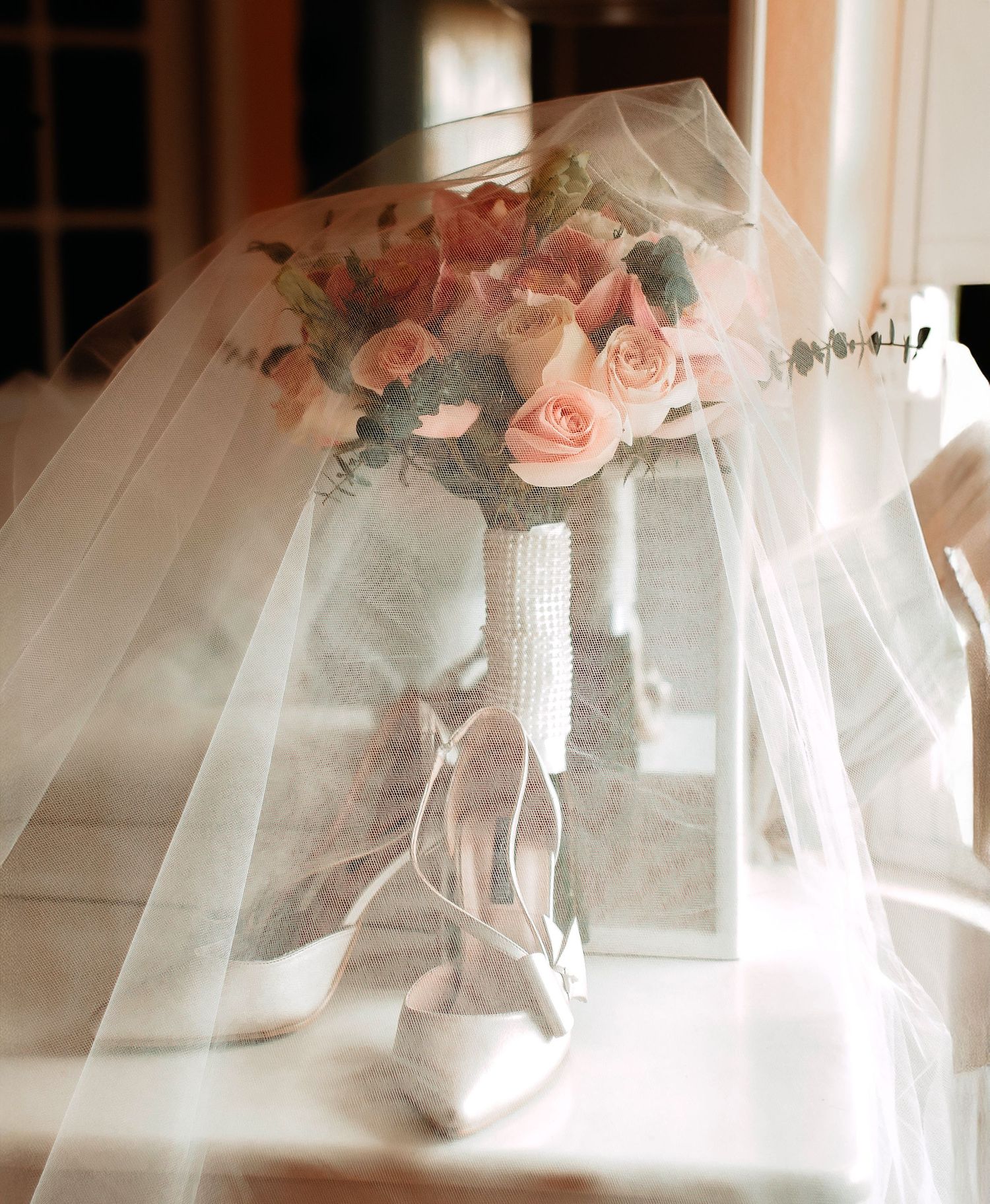 Wedding bouquet with pink roses and bridal shoes draped with sheer veil.
