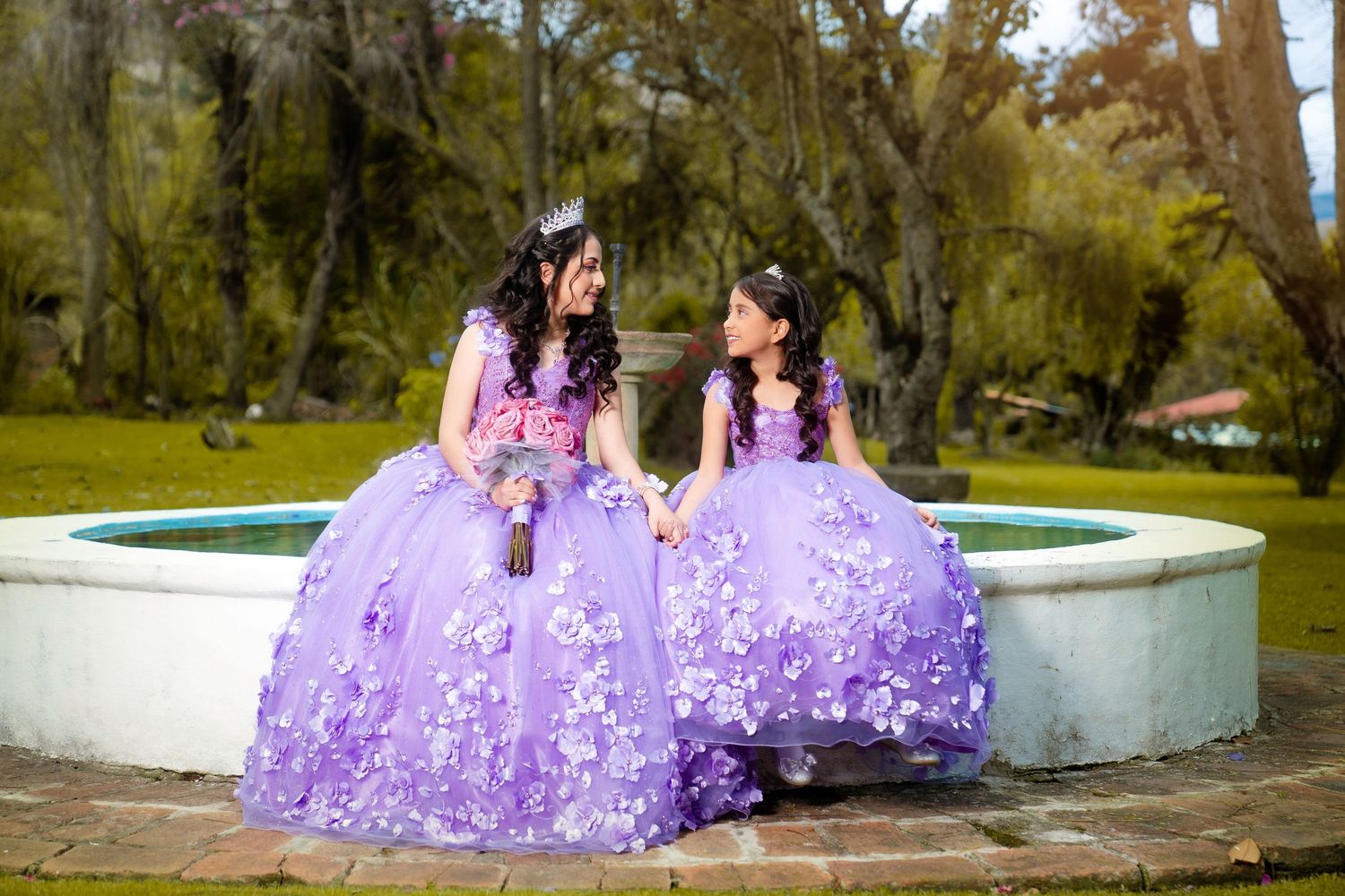 Group wearing matching purple quinceañera gowns poses elegantly in a garden setting for formal portraits.