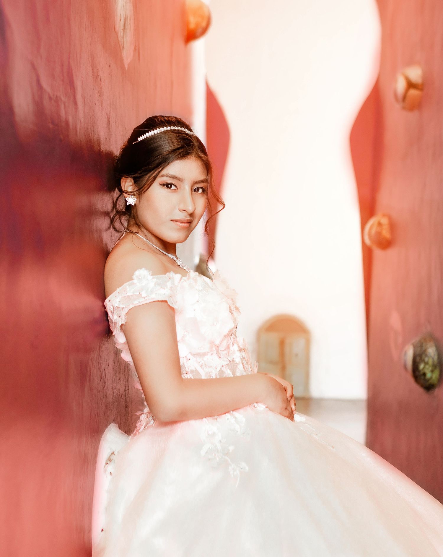 Portrait in pink ballgown with off-shoulder design against coral-colored background.