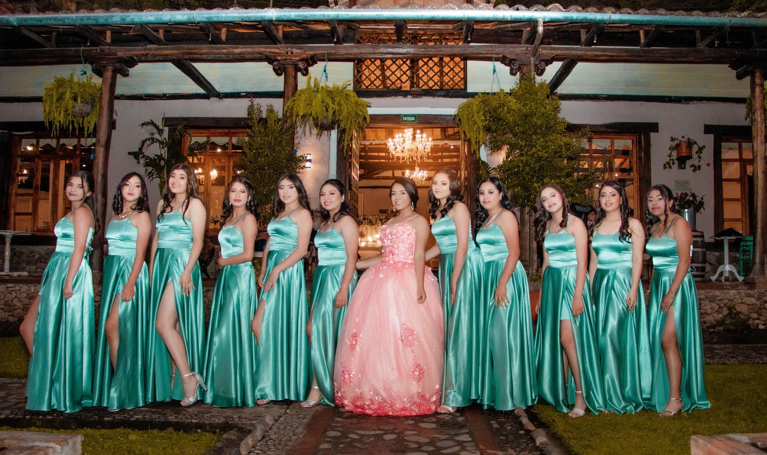 Wedding party in teal bridesmaid dresses and pink gown poses outdoors at sunset.