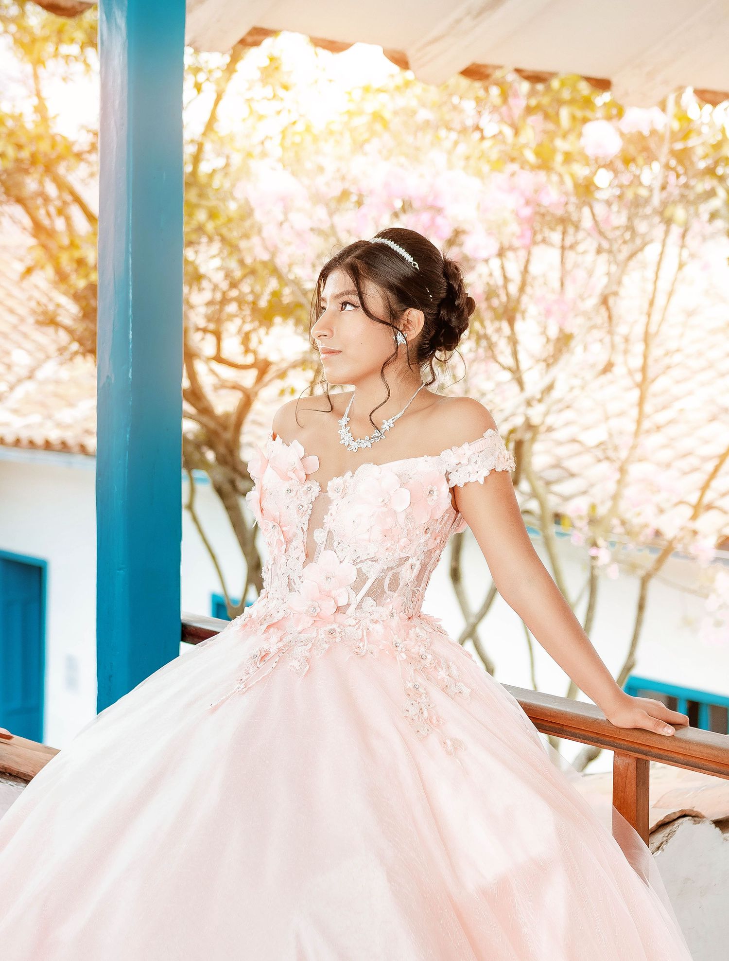 Portrait in pink princess gown posing on balcony with sunlit background.