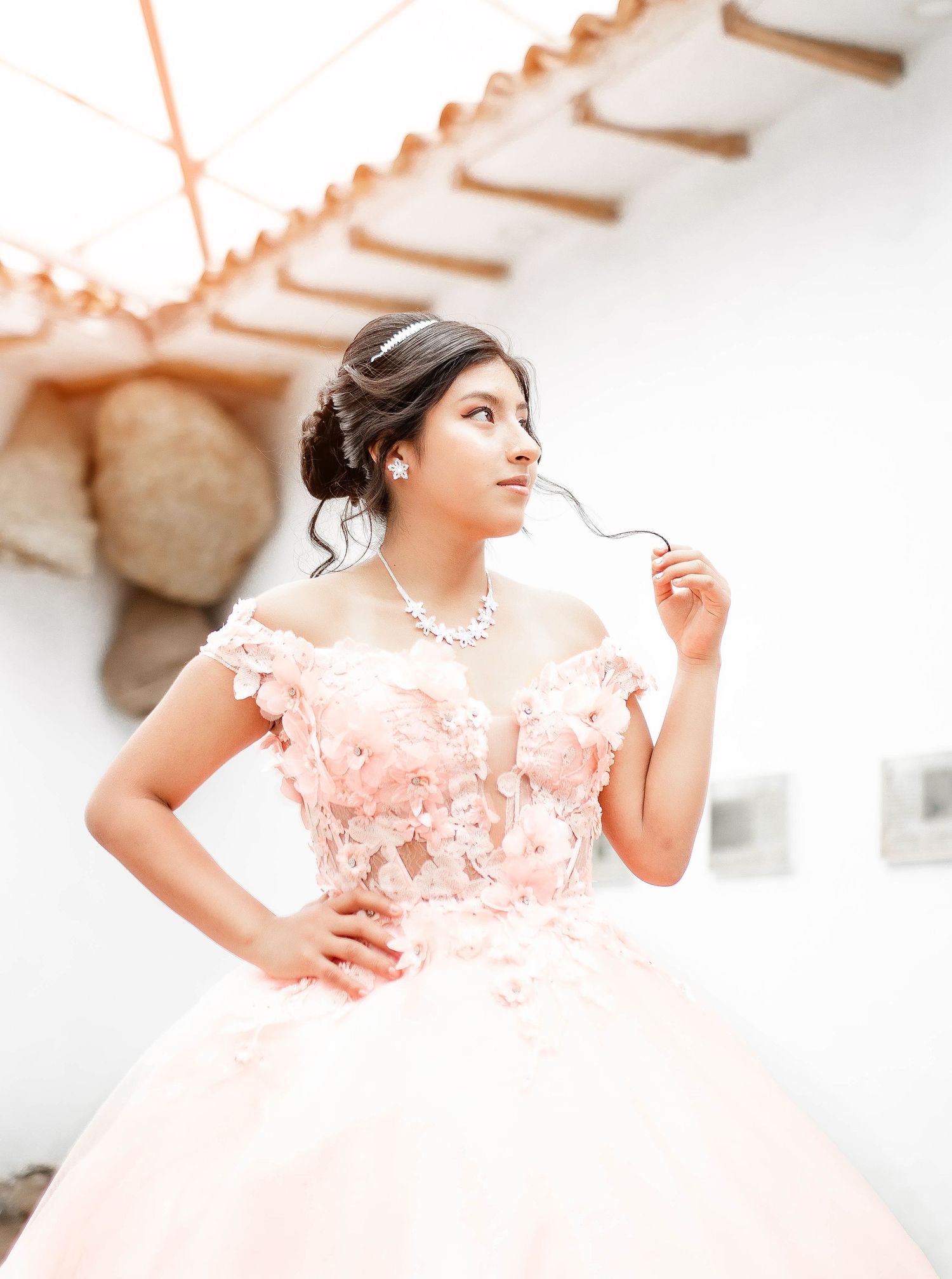 Elegant portrait in pink gown with off-shoulder neckline against white architectural background.