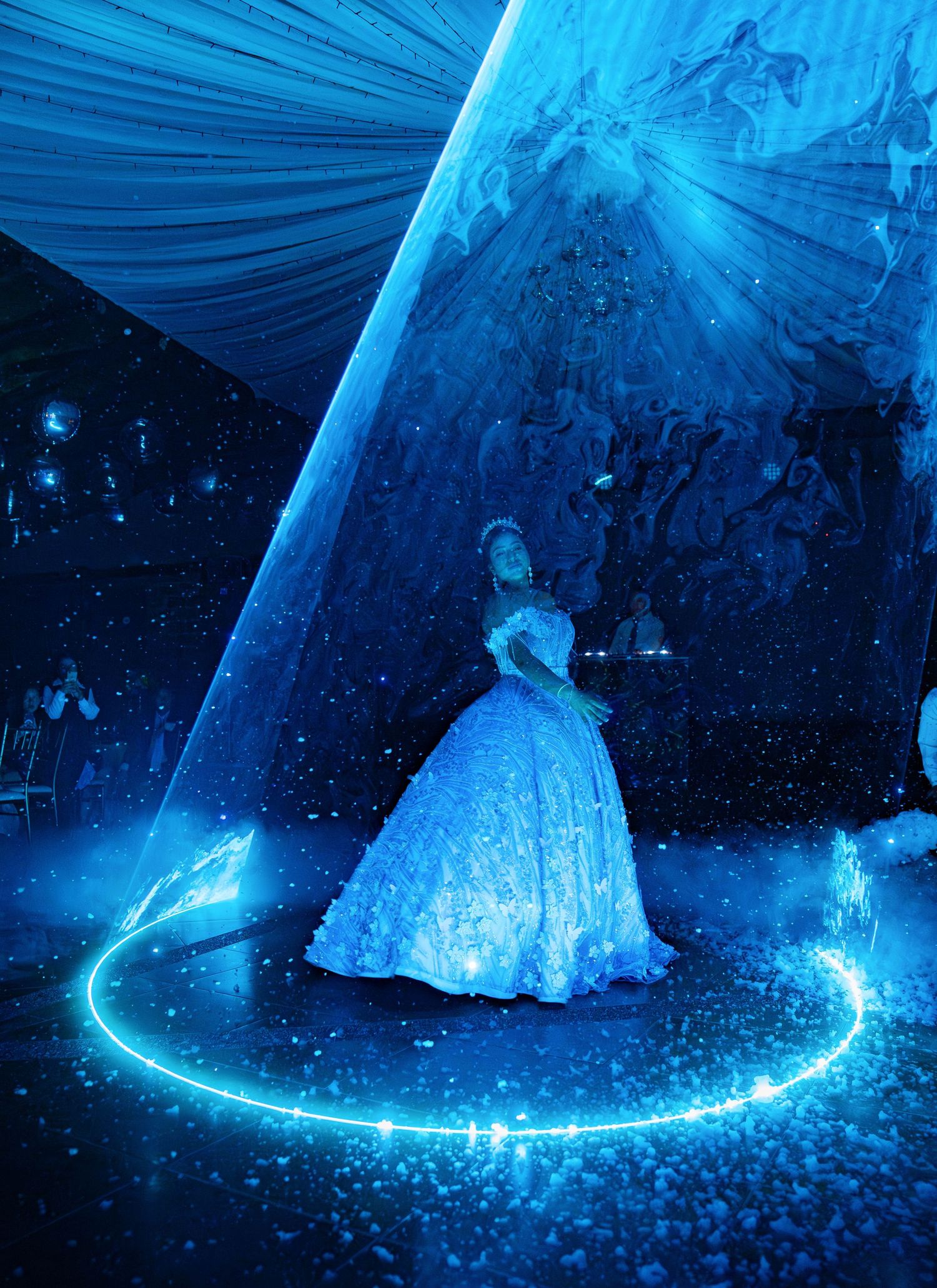 A figure in a glowing blue ballgown stands in a magical swirling light circle amidst a starlit ethereal backdrop.