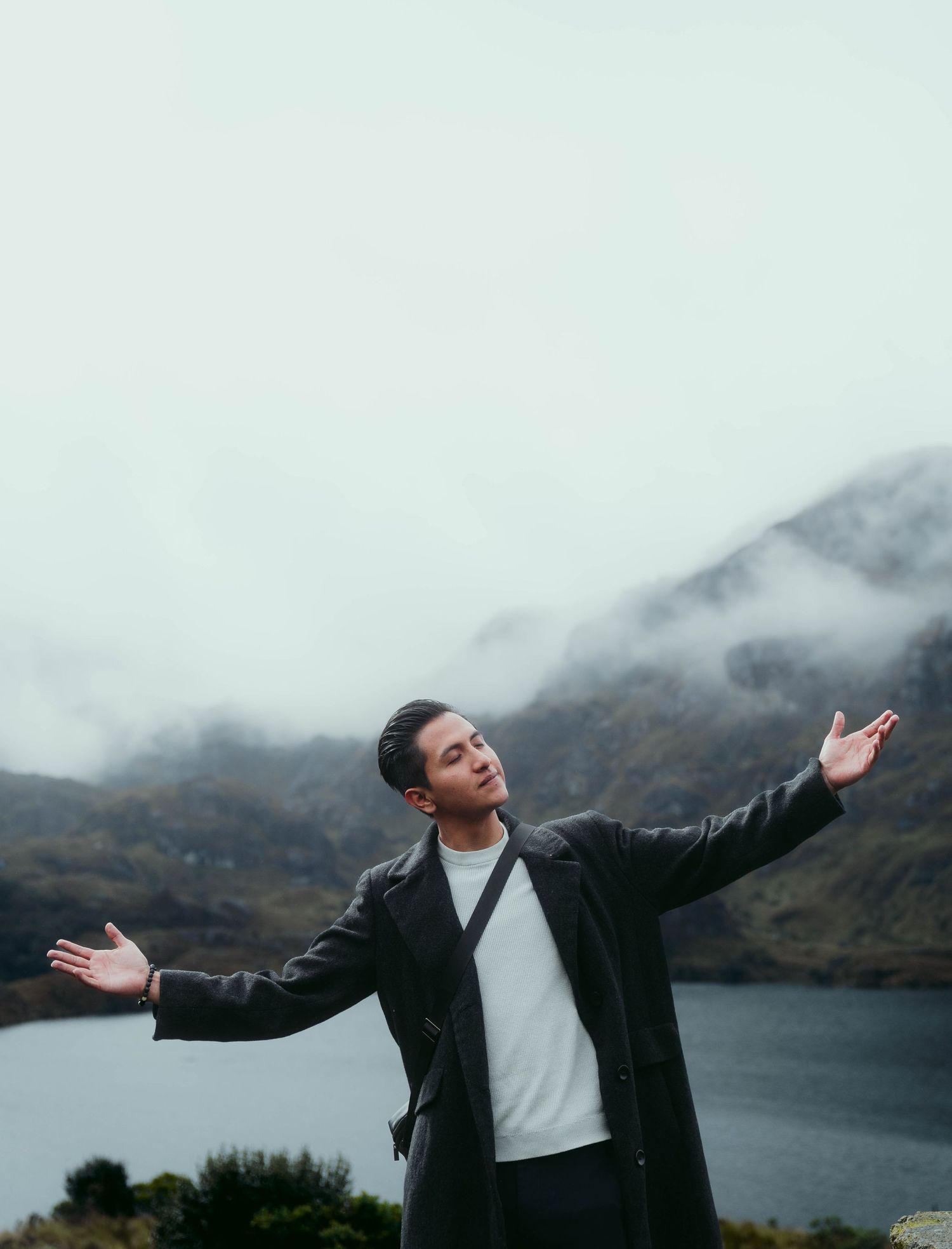 Dramatic portrait of person with arms outstretched against misty mountain lake backdrop.